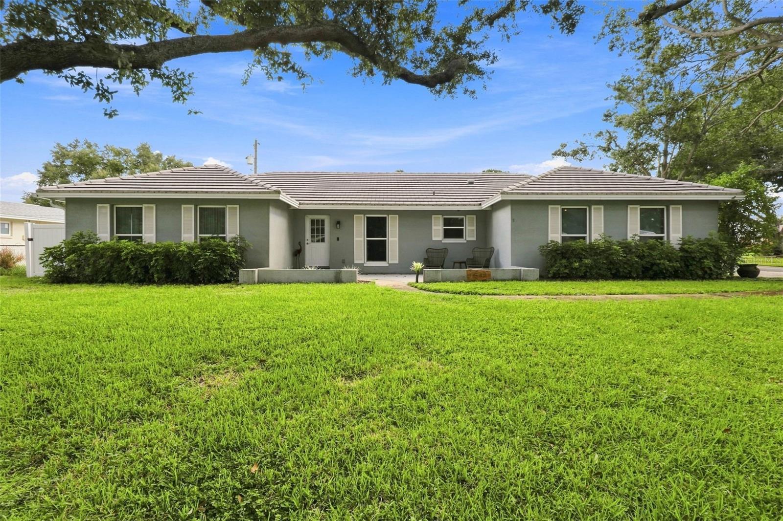 Space, flexibility, and a central Clearwater location come together in this 3-bedroom, 2-bath home offering approximately 1,820 square feet on a tree-shaded corner lot. Mature oak trees and a covered front porch create an inviting entrance, while the split-bedroom floor plan provides privacy and comfortable separation between living spaces. Inside, separate living and family rooms offer room for entertaining, relaxing, or creating distinct areas for everyday life. A dedicated dining area with glass-paneled French doors adds character, and an additional office or flex space provides options for working from home, hobbies, or overnight guests. The kitchen features white cabinetry, contrasting countertops, a tile backsplash, and a breakfast bar that opens to the family room. Warm flooring carries throughout the main living areas and bedrooms, giving the interior a comfortable, cohesive feel. Sliding glass doors lead to a spacious enclosed porch filled with natural light and overlooking the fenced backyard—an ideal extension of the home for casual gatherings or quiet mornings. The backyard includes a double gate for added access, while the side-entry garage provides additional functionality. Conveniently located near shopping, restaurants, medical facilities, downtown Clearwater, Coachman Park, Clearwater Beach, and Pier 60, this property offers generous space and easy access to the experiences that make Clearwater living so appealing.