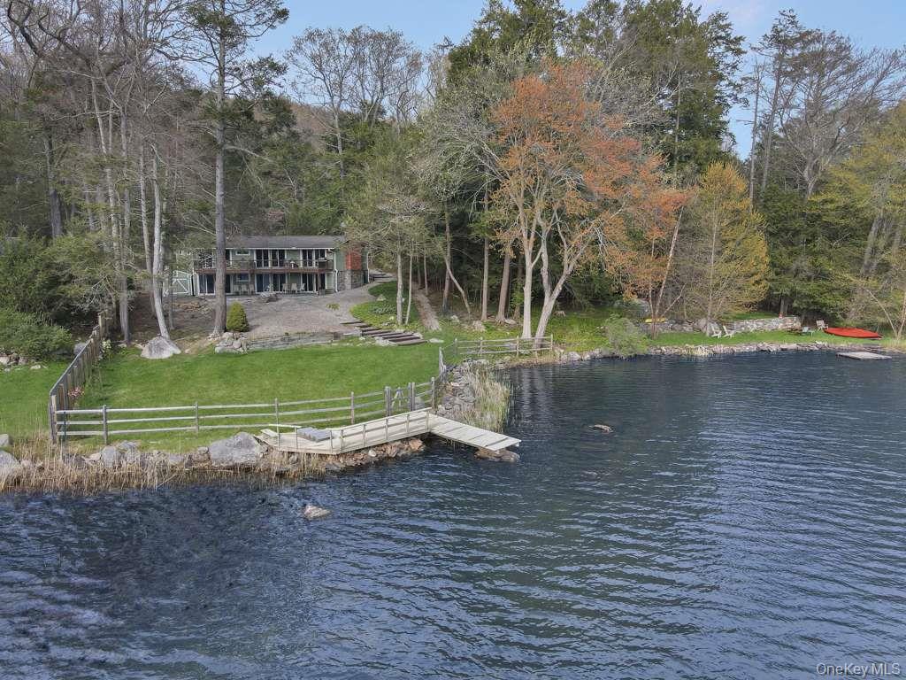 Set along the shoreline of Lake Oscaleta, this direct waterfront home offers a rare combination of privacy, natural beauty, and truly usable lakefront property in the heart of South Salem. Occupying .564 acres with sweeping frontage on one of the area’s most peaceful glacial lakes, the setting is defined by something increasingly hard to find - an expansive, level lawn that extends all the way to the water. Unlike many lakefront properties where steep slopes limit access and usability, this property offers a broad, open yard ideal for entertaining, recreation, or simply enjoying the outdoors. The gentle approach to the lake creates an effortless connection between the home and the water, making everyday use as practical as it is beautiful. At the shoreline, a substantial private dock and swim platform provide immediate access to the lake, whether for launching kayaks and paddleboards or spending long summer days in and around the water. Lake Oscaleta is known for its depth and quiet character, with limited motorized use that preserves its calm, reflective setting. The home itself has been thoughtfully updated and is designed to maximize its connection to the lake. The main level, offering approximately 1,578 square feet, is centered around an open living and dining space with vaulted, wood-beamed ceilings and a striking brick fireplace that anchors the room. Walls of glass and sliding doors frame the water from nearly every angle, filling the home with natural light and providing seamless access to the expansive deck - perfect for dining, entertaining, or simply taking in the view. The kitchen integrates comfortably into the living space, creating an easy flow for both everyday living and gatherings. The primary bedroom enjoys direct access to the deck and lake views, while two additional bedrooms and well-appointed baths complete the main level. The home is also equipped with an automatic whole-house generator, providing peace of mind and uninterrupted comfort year-round. The full walkout lower level adds approximately 1,200 square feet of flexible living space, ideal for guests, recreation, or extended stays. With its own fireplace, multiple seating areas, and direct access to the stone patio and backyard, it functions as a true extension of the home, offering both comfort and versatility. Outside, the landscape has been designed to complement the natural setting, with a combination of lawn, stonework, and mature trees creating multiple outdoor living areas without sacrificing the openness of the yard. From the elevated deck to the covered patio below, every space is positioned to take advantage of the lake. Just minutes from the hamlets of South Salem and Ridgefield, and within easy reach of Metro North and major highways, this is a property that offers both escape and accessibility. A rare opportunity to own a level, highly usable waterfront property with a substantial dock on one of Northern Westchester’s most serene lakes.