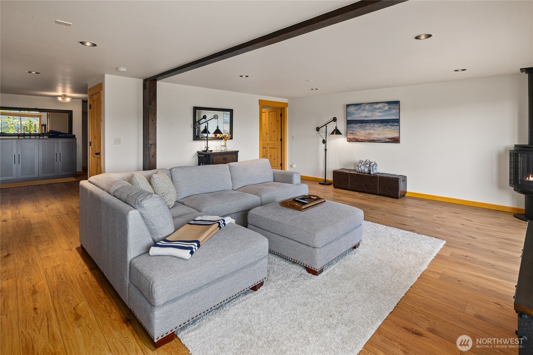 Comfortable lower-level gathering space with wood flooring, exposed beam accents, and a freestanding propane stove.