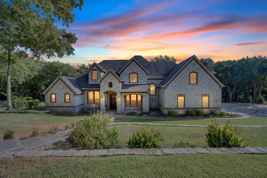 Luxury living at Stone Creek Farms, one of Aledo's most elite gated communities! Nestled beneath a mature tree canopy on an expansive 1.364-acre creek lot, this magnificent two-story stone and brick estate seamlessly pairs English architectural elegance with serene Texas landscape. Step inside the grand foyer boasting rich hardwood flooring, soaring ceilings, wainscotting, and exquisite trim work that leads you through a thoughtful floor plan featuring 4 spacious bedrooms and 4.1 designer baths. Working from home is a dream in the executive study set behind classic French doors with custom built-ins, while host-ready spaces abound—including a formal dining room, sunny breakfast nook, integrated intercom system, and three cozy stone fireplaces. The heart of the home centers around a breathtaking ivory chef’s kitchen featuring custom cabinetry, granite, a prep island, gas cooktop, double ovens, built-in desk, butler’s pantry, and views into the coffered family room. Indoors, entertain with a plush private media room, an upstairs game room with a wet bar and mini-fridge, and a primary suite retreat with a double-sided fireplace and spa bath. Auto enthusiasts will love the 3-car NASCAR garage painted with American and Texas flag cabinetry, sleek epoxy floors, hexagonal LED lighting, and built-in storage. Outside, step into a resort-style paradise surrounded by lush tropical landscaping, banana plants, and flagstone hardscaping. Relax on the covered brick patio or dive into the curved infinity-edge pool with a diving board, water fountains, and stacked-stone spillover spa. Gather on the sunken stone terrace around the built-in gas fire pit with bench seating framed by oak trees and forest views. High-and-dry peace of mind comes built right in thanks to an advanced, highly efficient drainage system. The home also includes an owned security system and CCTV monitoring system. New high-impact shingle roof in 2025 and Generator and Culligan Water system installed 2024.