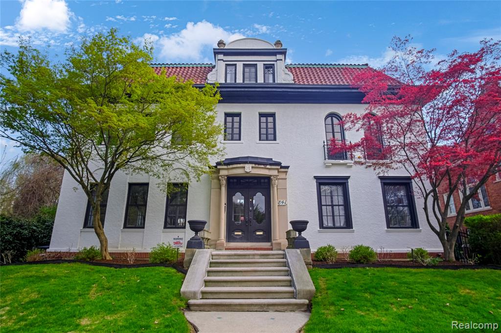 Built in 1921, 841 W Boston is a refined Mediterranean Revival set on one of Boston Edison’s most architecturally consistent blocks. White stucco, red clay tile roof, and a limestone entry with pilasters create a strong, formal presence, framed by mature landscaping and Japanese maples. Inside, a marble foyer opens to a dramatic stair with wrought iron balustrade, wood handrail, and brass accents, leading to a gallery-style upper landing with statement chandelier. The main level offers large, well-scaled rooms with original millwork, crown molding, and casement windows, anchored by a carved marble fireplace with updated wood-burning insert, along with a standout sunroom wrapped in original Pewabic tile and natural wood trim. The kitchen is fully renovated with a Bertazzoni range, marble waterfall island, custom cabinetry, brass hardware, and butler’s pantry, opening to a bright breakfast nook. The second floor includes four bedrooms, including a primary suite with arched French doors, along with two full and one half bath, including a preserved period tile bath. The third floor offers two additional bedrooms, a full bath, and a large-scale flex space currently configured as a media and recreation room. The first floor includes a speakeasy-style entertaining space with exterior access. The grounds offer a deep, fully usable lawn and a defined brick patio for outdoor living, while a fully rebuilt carriage house functions as a separate residence with its own kitchen, bath, and bedroom, supported by a multi-zone mini-split system. Recent improvements include full landscaping, complete carriage house renovation, exterior stucco repair and repainting, underground sprinkler system installation, and roof tile repairs, completing a clean, intact example of Mediterranean Revival architecture with scale and presence.
