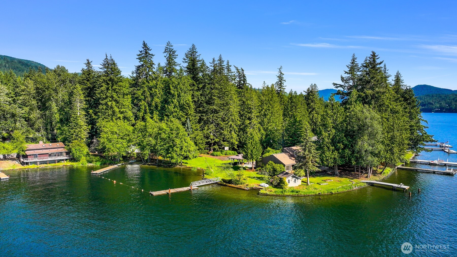 Tucked along the sunny eastern edge of Lake Whatcom sits this exceptional private estate. Comprising 3.1 private acres of flat, usable land, the property features nearly 900 feet of low-bank sandy shoreline—an increasingly rare amount of direct, effortless lake access. The west facing orientation, with unobstructed exposure delivers sunlight from dawn through the long, cinematic sunsets that define life on Lake Whatcom. Three docks and a dedicated boat ramp ensure seamless launch points for whatever vessels or watercraft suit the season, while the generous moorage invites both serious boating and spontaneous summer afternoons. At the heart of the estate are two primary residences. The main home is a refined contemporary with three bedrooms and two-and-a-half baths, designed to frame sweeping 180-degree lake views from nearly every room. Positioned on its own private peninsula, it showcases timeless modern lines with unparalleled potential. Steps away, at the water’s edge, rests the second home—a warmly appointed two-bedroom, two-bath home with loft, perfectly suited for guests or simply changing the daily perspective. Four additional historic cabins complete the offering, one of which has been thoughtfully finished and used as an ADU. Together they create layered possibilities: a true multi-generational compound, thoughtful income potential, or flexible space for a weekend escape. One of a kind would be an understatement for this rare property.