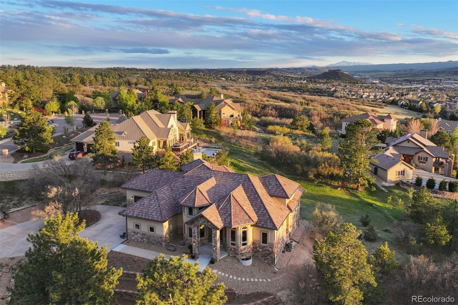 With panoramic Front Range views, Pikes Peak and “The Rock” in full sight, and a private position within Piñon Soleil, this home feels open to the horizon, yet sheltered in its setting. Every space is oriented to the surrounding landscape, creating a natural rhythm between indoors and out. With convenient access to Castle Rock, Parker, and Denver, dining, shopping, and daily essentials are always within easy reach.Curved walls, soaring ceilings, and rich layers of timber, stone, and brick create a sense of warmth and character. Double-arched front doors open to a sunlit foyer and great room, where a two-sided fireplace and walls of glass frame the mountain views. Cherry floors carry you through the main level and into a chef’s kitchen featuring high-end appliances, a generous island, a walk-in pantry, and a brick fireplace that naturally draws people in. Surrounded by windows, the eat-in area feels relaxed for daily living, while the formal dining room offers an elegant setting for hosting.This home offers the flexibility of two spaces that could serve as a primary suite, depending on how you live. The upper level provides a serene retreat with a private balcony, dual walk-in closets, a fireplace, and a spa-like bath. A clawfoot tub rests within a turreted bay window, perfectly positioned to take in the views. On the main level, a guest suite with its own five-piece bath and mountain outlook offers an equally comfortable option for main-floor living or long-term guests.The walk-out lower level is designed for entertaining and everyday enjoyment, with a spacious recreation room, wet bar, theater, and dedicated gym space. Outside, the flat backyard opens up new possibilities, from a future pool or garden to simply enjoying the space as-is. A four-car garage, circular drive, and additional parking add convenience. This is Colorado living at its most refined, elevated, private, and designed for a life well lived.