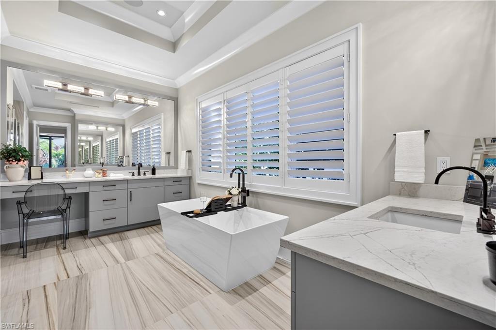 Full bathroom featuring two vanities, a soaking tub, a tray ceiling, ornamental molding, and recessed lighting
