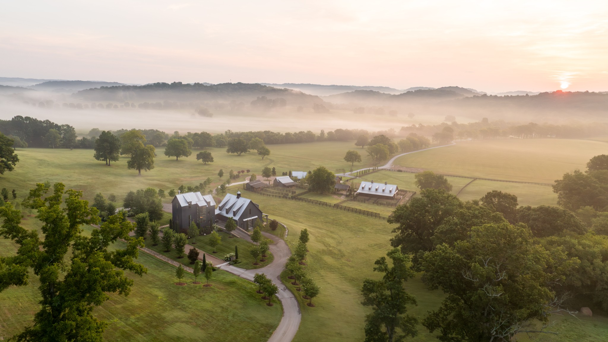 Nestled just two miles from the heart of historic Leiper’s Fork, Little Fawn Farm encompasses 97 acres of exquisitely maintained countryside along one of Middle Tennessee’s most prestigious roads. A grand entry gate sets the tone, welcoming visitors into a property defined by meticulous attention to detail and timeless Southern charm. As you wind down the long drive, passing a tranquil pond with a fountain, you’re enveloped by sweeping views of rolling pastures and wooded ridges. The main residence, a charming three-bedroom home designed to capture natural light, sits perfectly elevated to take in the scenic vistas. The entire third floor is dedicated to a luxurious primary suite offering unobstructed views for miles. Entertaining is effortless here, thanks to a stunning 35x40 party barn. Once a working barn, it’s been transformed into an entertainer’s paradise featuring multiple sitting areas, TVs for game days, a loft area, half bath, and kitchen. Glass bay doors open wide to let in the crisp Tennessee air, while a covered porch overlooks the new horse barn and beautifully fenced pastures. An inviting firepit and newly installed outdoor kitchen complete the barn’s alfresco offerings. For equestrian enthusiasts, the horse barn surpasses expectations with custom-built 14x14 stalls, indoor and outdoor wash bays, office, and a well-appointed tack room. Additional structures include a dedicated donkey barn, a spacious 30x50 detached four-bay garage ideal for a car collection, small barn with half bath and a workshop garage. The estate’s grounds boast natural water features like a spring-fed, stocked pond and a stunning swimming hole with stone coping, a waterfront fire pit and graceful waterfalls. The property enjoys frontage on Murfrees Creek for fishing, while deer and wild turkey are bountiful for the outdoor enthusiasts. Little Fawn Farm offers ample opportunities for expansion with an approved 12-bedroom perk site and three additional build sites.