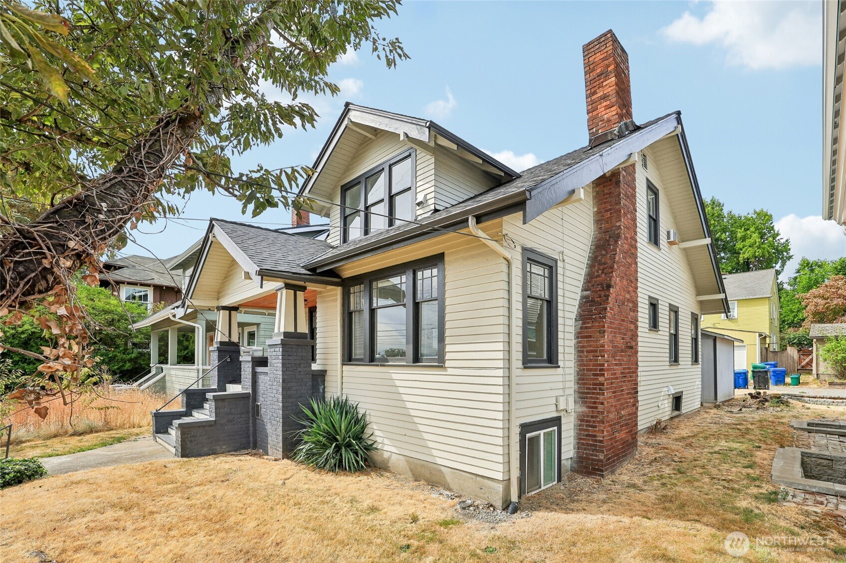 4545 5th Ave NE is a multi-level Seattle home built in 1919, with a covered front porch and several distinct living spaces. The main kitchen has stainless steel appliances, white cabinetry, and an adjacent dining area. A fireplace anchors the main living room, while wide openings connect the shared living spaces. The upper primary bedroom includes a walk-in closet, and an upper bathroom has a tub with a shower. Additional rooms and a kitchenette extend the layout on the lower level. The rear yard includes a detached storage structure. The home combines defined rooms with connecting living areas across its levels.