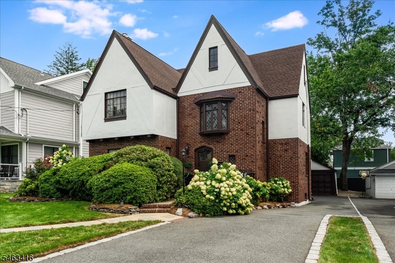Steep gables, rich brickwork and classic architectural details give this Tudor a distinctive elegance on a quiet, picturesque street. An entrance vestibule opens to a gracious hall, where a sculptural winding staircase, finely detailed woodwork and a graceful window seat beneath diamond-paned leaded glass create a dramatic architectural focal point. The gracious living room pairs a wood burning fireplace w beautifully detailed built-in shelving and cabinetry, a refined backdrop for favorite books and collected pieces. Through an arched opening, the elegant dining room sets the scene for lingering dinners. A newer kitchen with ss appliances and breakfast bar welcomes morning coffee and casual meals. Beyond, the large, sunlit family room offers space to stretch out, gather for movie night or host a crowd. Two sets of French doors open to the yard, taking the party outdoors. Upstairs, the bright and airy primary suite features a high tray ceiling, arched windows, generous closets and storage, a window seat for quiet reading, and an en suite bath. Three additional spacious bedrooms and a hall bath complete the floor. A finished LL with a full bath offers room for recreation, exercise or work. Lush landscaping surrounds a patio and yard for alfresco dinners, relaxed conversation and a sheltered lounge. Only .4mi to NYC train and v close proximity to all schools, downtown shops, and restaurants makes coffee in town, dinner out and the daily commute part of an easy everyday rhythm.