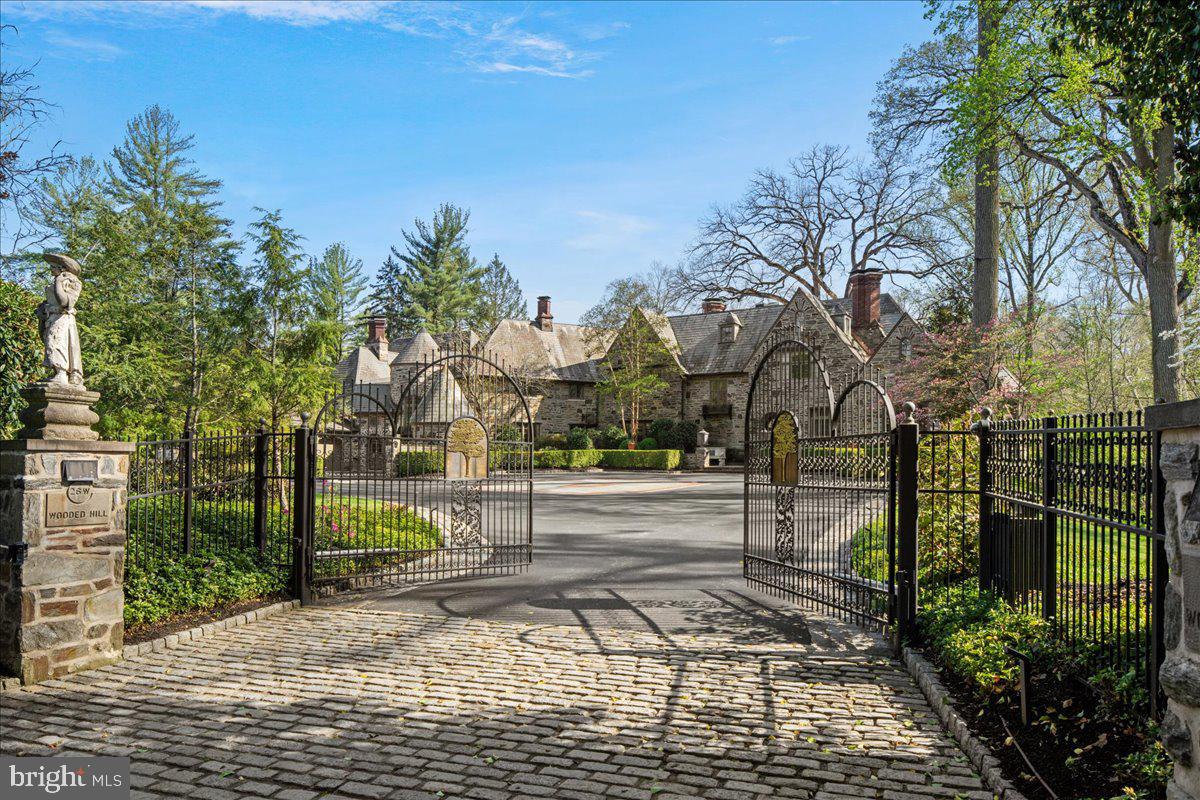 Privately tucked behind gated stone piers in Gladwyne, “Wooded Hill” unfolds across nearly seven acres of lush, mature grounds designed for both quiet seclusion and outdoor enjoyment. Expansive lawns, formal gardens, winding stone paths, and a pool with pavilion create a setting that feels more like a private retreat than a traditional residence. A dedicated golf green with multiple tee boxes and a series of terraces further extend the outdoor living experience.At the center of the property sits a 16,410-square-foot residence that blends historic character with extensive modern upgrades. Natural light pours in from every angle, highlighting detailed craftsmanship such as custom millwork, decorative iron accents, intricate ceiling designs, and seven fireplaces. French doors throughout the home open to the surrounding landscape, reinforcing the connection between indoor and outdoor spaces.The home is equally suited for large-scale entertaining and everyday living. Gathering spaces include formal living and dining rooms, a sunroom, a billiards room, and multiple family rooms, while two private offices provide flexibility for work or study. The kitchen, positioned as a central hub, is paired with a bright breakfast area for casual dining.A private primary wing offers a retreat within the home, complete with dual spa-like baths, a sitting area, and a balcony library overlooking a dramatic two-story family room. Additional bedroom suites—each with walk-in closets and private baths—are complemented by a second-floor library. Altogether, the property accommodates eight bedrooms, including a fully independent two-bedroom apartment ideal for extended stays or live-in support.The lower level expands the home’s recreational offerings with a theater featuring tiered seating, a fitness room, a custom bar, and direct access to the outdoor entertaining areas.A separate guest house, thoughtfully renovated with a more contemporary aesthetic, provides two additional bedrooms and a sense of privacy for visitors, accessible through a charming stone courtyard.Modern infrastructure supports the estate’s scale and convenience, including a whole-house generator and an integrated smart home system controlling lighting, security, audio, and pool functions.Despite its secluded setting, the property is just minutes from local village amenities, King of Prussia, Center City Philadelphia, and major transportation routes—offering both privacy and accessibility in one of the Main Line’s most desirable locations