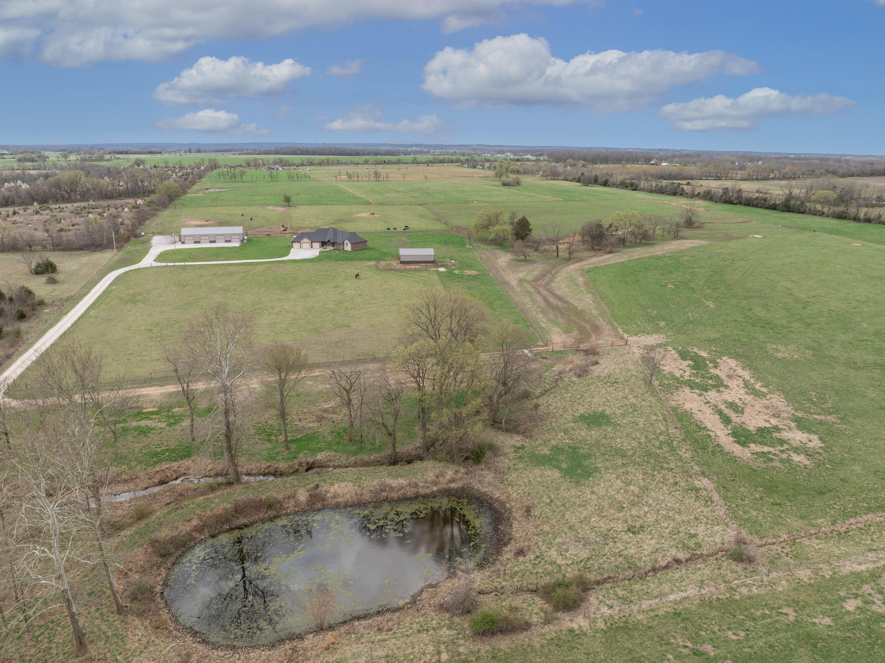 Behind a gated entrance on a paved county road, this stunning 80-acre farm features a custom all-brick 3BR, 2.5BA Home with a split floor plan and spacious, thoughtfully designed living areas.  Enjoy a Formal Dining Room, Office/Bonus Room and a bright Sunroom with cathedral ceiling, gas fireplace and peaceful pasture views.  The Living Room offers a vaulted beamed ceiling, stone fireplace and built-ins, while the beautiful Kitchen impresses with granite counters, alder cabinetry, GE Smart Cafe appliances (including a fridge with built-in Keurig), a Wolf 6-burner propane cooktop, large island, walk-in pantry, wine/beverage cooler, mixer lift, pull-out pot drawers and hidden storage.   The luxurious Master Suite features a scalloped tray ceiling, ambient lighting, spa-like bath with granite double vanities, soaking tub, walk-in shower and oversized custom closet.  Two additional Bedrooms and a Full Bath are located on the opposite wing for added privacy.  Other highlights include engineered hardwood, LVP, tile, carpet, a screened-in back porch, and a utility wing with mudroom-style entry, hall tree, Laundry Room and Half Bath.  The oversized, insulated, heated/cooled 3-car Garage includes a utility sink, mechanical room, storm shelter and electric dog door.  A 40'x80' Metal Shop offers 12' sidewalls, concrete floors, 6 overhead doors (4 are 12'x10'), floor drain and full LED lighting.  A 30'x40' LED-lit Pole Barn is set up for horses, surrounded by paddocks with high-tensile fencing.  Fertile, fenced and cross-fenced pastures (barbed & smooth wire) are livestock-ready.  Additional features: 2 ponds (one spring-fed), wet-weather creek, 5 frost-free waterers and a permanent pipe corral system for low-labor livestock handling.  This property blends luxury living with turnkey farm functionality ... ideal for cattle, horses, or mixed-use livestock.