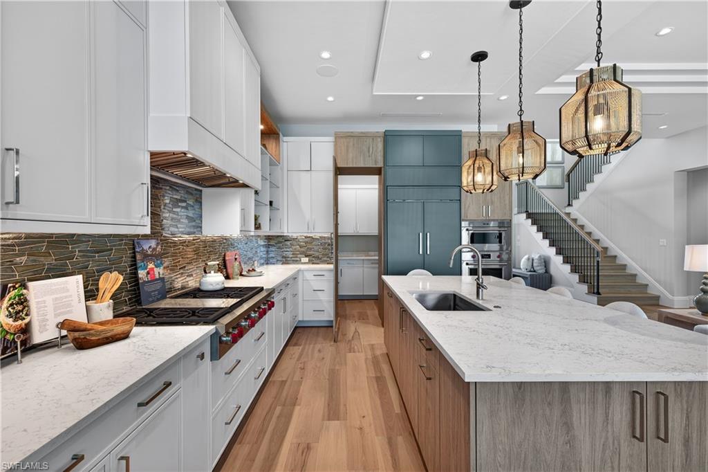 Dual tone kitchen with dual tone cabinets, light stone countertops, light wood-style flooring, pendant lighting, and modern cabinets