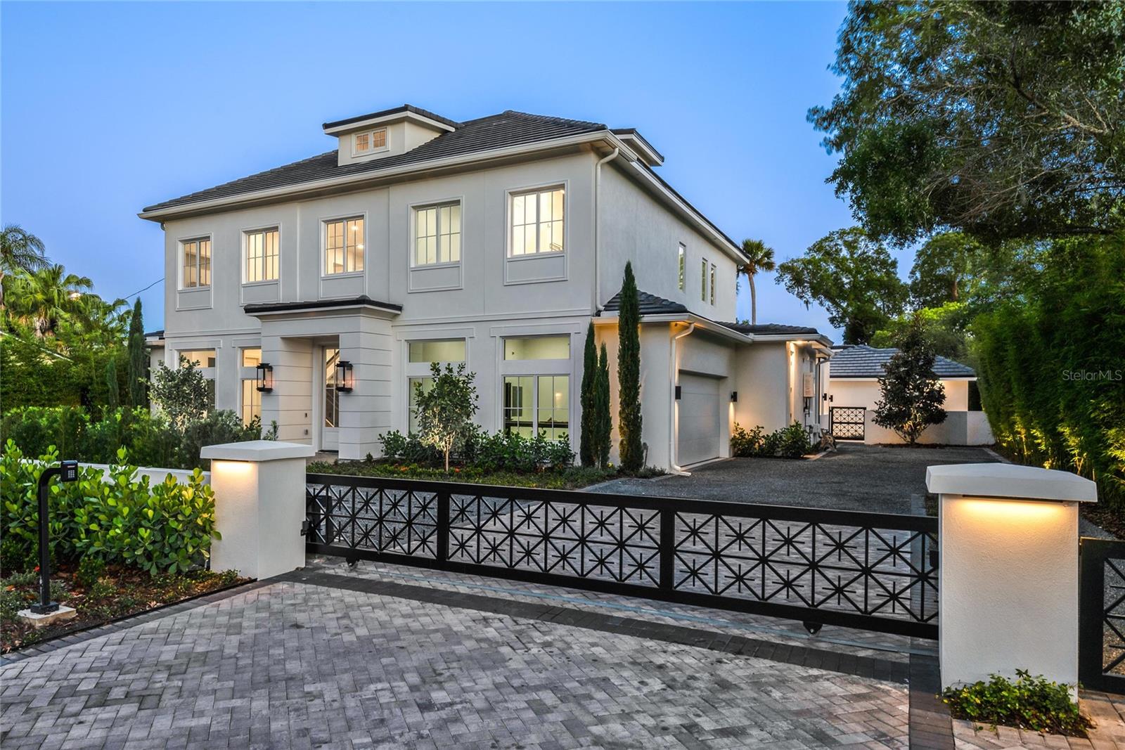 Experience refined luxury in this newly constructed 2024 Hamptons-style residence, a seamless blend of elegance and modern sophistication. A remote-operated gated entrance opens to a grand circular driveway and private motor court, setting the stage for this exceptional estate. The two-story foyer impresses with a glass-paneled staircase that wraps around a temperature-controlled wine room and a transparent glass elevator, effortlessly connecting all levels, including an expansive third-floor multi-purpose retreat. Designed for contemporary living, the thoughtfully curated floor plan features a spacious open-concept gathering room with multiple French doors leading to a covered lanai. The dining area, framed by a striking glass wall, overlooks a serene backyard with a sparkling pool and spa. The main residence offers four private bedroom suites, complemented by a detached pool cabana that serves as a fifth bedroom or versatile guest retreat. A hidden office, den and an expansive upstairs lounge provide flexible living spaces ideal for a media room, bar or billiards area. The gourmet kitchen is an entertainer’s dream, featuring dual 10-foot stone islands, a 60-inch Wolf range, dual 36-inch Sub-Zero refrigerator and freezer columns, a warming drawer, beverage center and a 146-bottle Sub-Zero dual-zone wine cooler. A separate pantry kitchen is equipped with a Dacor induction cooktop, convection oven, additional refrigerator, microwave, dishwasher and ample cabinetry, ideal for catering and meal preparation. The first-level primary suite is a tranquil retreat, offering a sitting area, an all-marble bath with a glass-enclosed shower, multiple body sprays, a soaking tub, and French doors leading to a secluded Zen garden with an outdoor shower and fountain. The second level hosts three additional bedrooms with en suites, a generous family lounge, a bar, a full bath and a well-appointed laundry room with extensive cabinetry. The third level, accessible by the staircase and elevator, offers nearly 770 square feet of adaptable space. Outdoor living is elevated with a spacious lanai featuring motorized screens, a gas fireplace, dining space, and a summer kitchen with a 54-inch Coyote wood and gas grill, plus a separate burner beneath a remote-controlled louvered roof. The detached cabana offers flexibility as a guest suite, fitness studio, additional office or game room, complete with a full bath, mini kitchen, and washer/dryer. Crafted with meticulous attention to detail, this home showcases Anderson windows, 10-foot solid doors, high-end plumbing and electrical fixtures, and Trane HVAC system, ensuring quality and comfort. Lush landscaping, including magnolia trees, bamboo and cypress, surrounds the property, creating a private sanctuary. An attached side-entry garage features a state-of-the-art car lift providing space for three vehicles. Ideally near Interlachen Country Club, Winter Park Racquet Club, Phelps Park/YMCA, and renowned Park Avenue, this exquisite estate offers an unparalleled lifestyle. Note: Partial staging by Restoration Hardware. The furnishings package can be purchased separately.