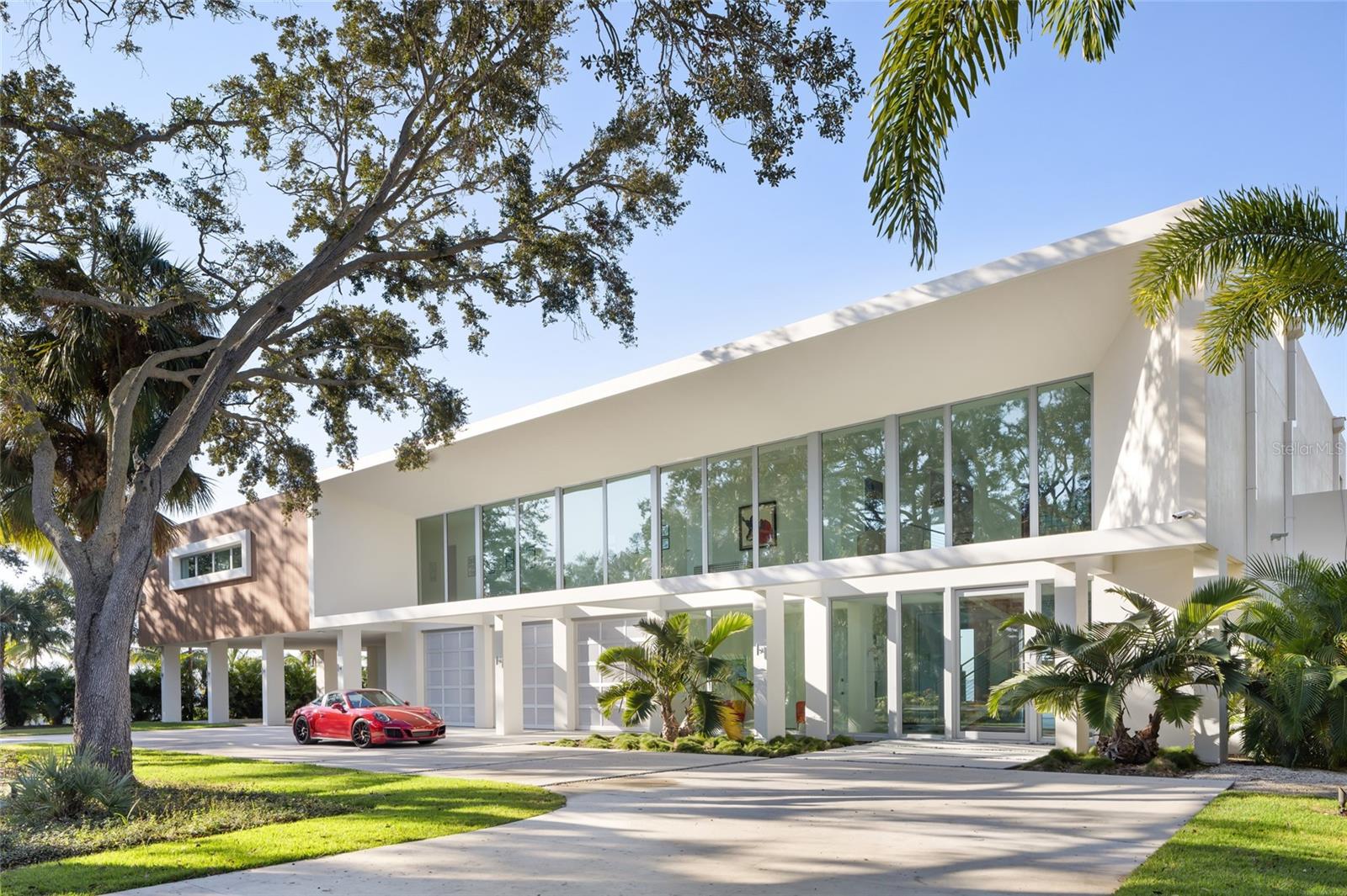 Exquisite Jewel on Sarasota Bay - A true statement of modern design and sustainable luxury, this contemporary masterpiece offers nearly 180 feet of frontage on Sarasota Bay with panoramic water views that seem to stretch endlessly. Designed by acclaimed DSDG Architect Mark Sultana and meticulously constructed by Voigt Brothers, this gated estate rests on over one acre in the coveted Indian Beach neighborhood—also known as Sarasota’s “Museum Area.” Elevated by massive columns, the residence appears to float gracefully above the landscape, offering open-air colonnades beneath and full protection from the elements. Built entirely of reinforced concrete—including the roof—this home combines durability with contemporary warmth through rich wood accents and vibrant architectural details. The concrete roof supports a robust solar array, allowing the property to operate entirely independent of the power grid. Inside, an oversized glass pivot door reveals a stunning suspended staircase with solid wood treads and elevator access to the main living level. The expansive great room opens seamlessly onto a vast covered terrace through floor-to-ceiling impact glass doors, framing breathtaking views of the Bay. The ultra-modern gourmet kitchen, featuring movable glass partitions, can transform from open-concept entertaining space to a private culinary haven. The primary suite, located on the south end of the home, captures the most captivating views of the Ringling Bridge and includes a private study. Along a gallery of floor-to-ceiling glass, four additional guest suites each open to a full-length veranda overlooking the Bay and Longboat Key. Spa-like bathrooms feature interior glass panels to continue the water views even indoors. On the ground level, enjoy a four-car garage, storage areas, bonus space, and a shaded patio overlooking the dramatic 60-foot heated wet-edge lap pool with unobstructed vistas of Downtown Sarasota and the surrounding islands. Perfectly positioned near Downtown Sarasota, St. Armands Circle, Lido Beach, and cultural landmarks like the Ringling Museum and Ca’d’Zan, this residence defines the pinnacle of coastal contemporary living—a private, solar-powered sanctuary that seamlessly blends architecture, technology, and nature.