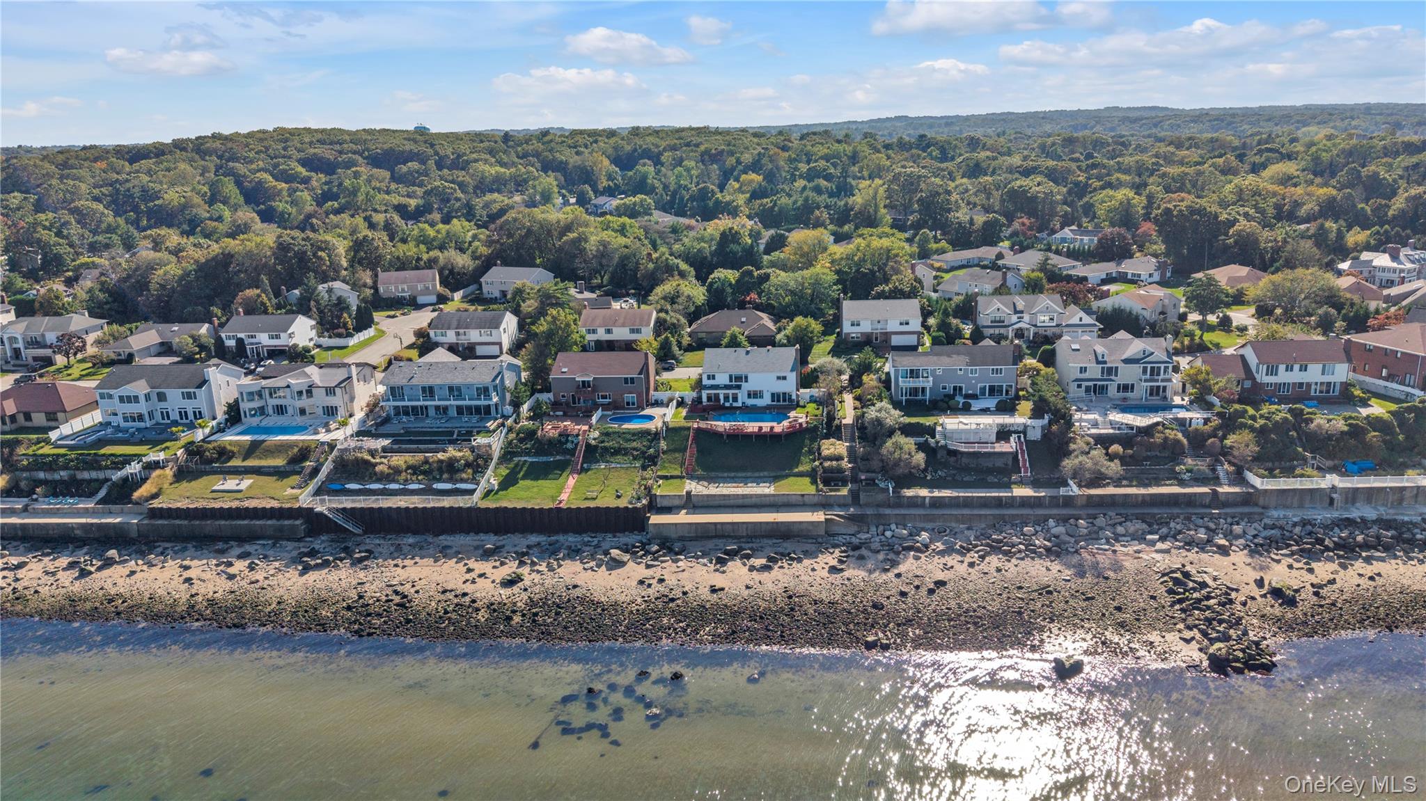 Direct waterfront property high above sea level in the Village of Bayville within the highly sought after of Oak Neck Point private community.  Sweeping panoramic views over the Long Island Sound, this property features steps down to a blue stone patio, additional sun deck and a private beach.  Sea wall in great condition. Water views upon immediately entering the home and from the backyard, absolutely stunning. This 5 bedroom colonial home has been updated throughout including heated granite floors and a beautiful Wood Mode Kitchen with custom cabinetry and bar open to a breakfast room and sliding doors to the backyard. Outside features an infinity style swimming pool blending into the horizon, outdoor shower, patio and deck.  Formal dining room and living room plus den with fireplace and custom built-ins round out the first floor.  The living and dining areas flow seamlessly to expansive glass doors that open to the backyard creating an unparalleled indoor-outdoor lifestyle ideal for entertaining or quiet relaxation on the water. Generously proportioned bedrooms, including a luxurious primary suite upstairs, big closets plus your own home office. The professionally landscaped grounds and direct waterfront setting create a private resort-like atmosphere, all just minutes from beaches, parks, local restaurants and close proximity to the towns of Locust Valley and Oyster Bay.