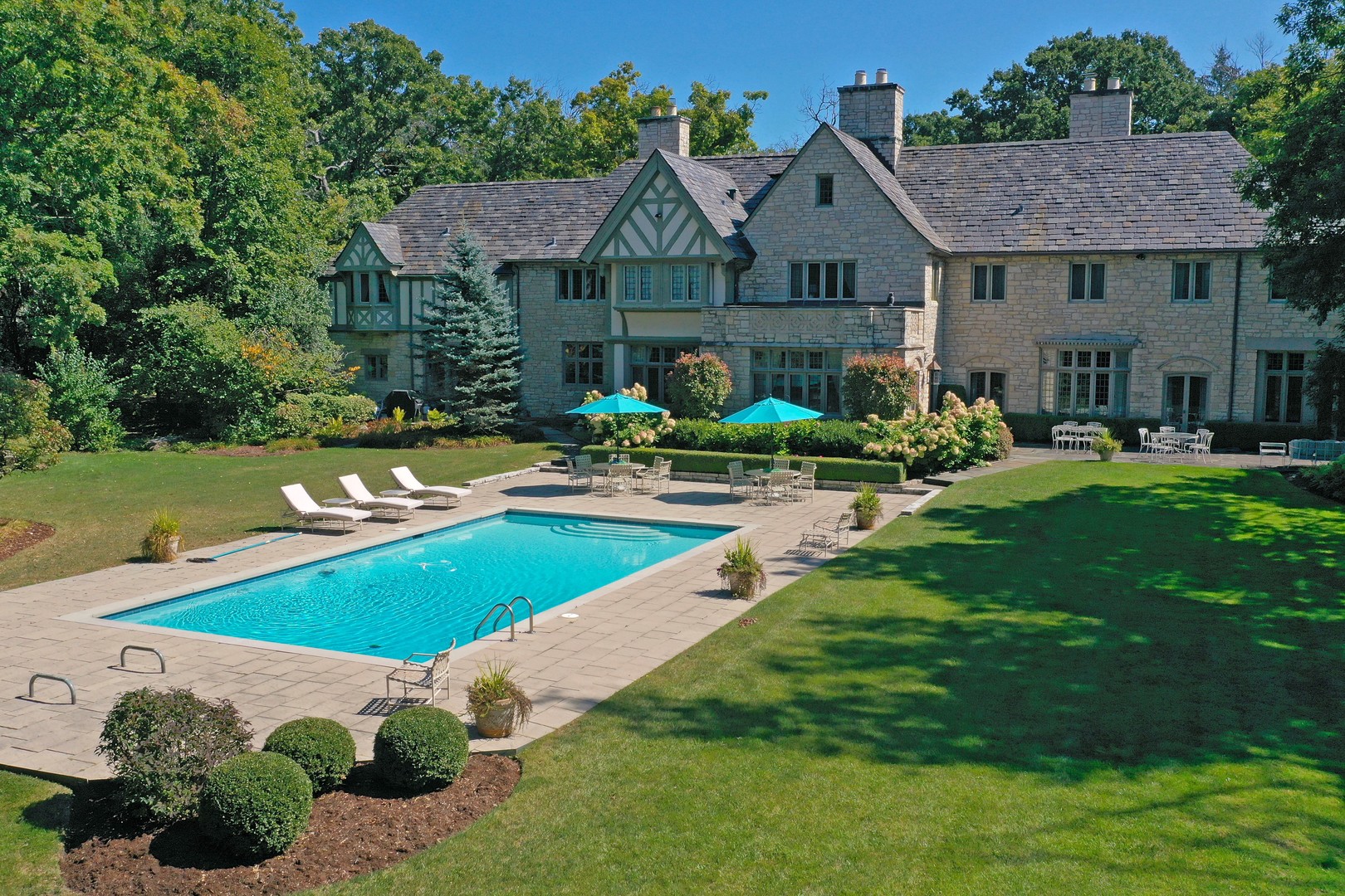 On the market for the first time in nearly 50 years, the historic Phelps Kelley House is one of Lake Bluff's most significant estate properties. Designed in 1927 by noted Chicago architect Ambrose Cramer, a protege of David Adler, this Tudor Revival masterpiece was originally part of the historic "Stonebridge" estate.   The 9.35-acre property is elegantly situated at the end of a long, private, tree-lined drive, and features a pond, rolling lawn, mature trees, gardens, a 7,383-square-foot main residence with meticulously preserved interiors, and a detached 5-car garage with a full coach house apartment above.  Across five decades, one family has carefully stewarded the character of this home, preserving its original grandeur through its stone floors, carved millwork, wood paneling, intricate moldings, tall casement windows, and generous ceiling heights. Cramer carefully planned the floorplan for gracious living and entertaining. A grand entry leads to expansive formal living and dining rooms-each with fireplaces and French doors opening to an expansive terrace overlooking verdant gardens and the pool beyond. A paneled sunroom offers a quiet retreat with views of the grounds and lends itself perfectly to a sun-filled private office. Service areas are thoughtfully configured for ease: a large butler's pantry with extensive vintage cabinetry connects the dining room to the kitchen, which adjoins a sunlit breakfast room oriented toward the pool. A spacious family room provides yet another vantage point to appreciate the property's natural beauty. Additional first-floor conveniences include a large laundry room, back staircase, and discreet storage integrated throughout.  Five bedrooms and six full baths complete the second floor, including a primary suite that functions as its own private wing with dual baths, multiple closets, and a dressing room rich with period character. Two additional bedrooms and 1.1 baths on the first floor offer ideal space for guests or multi-generational living. The lower level includes a powder bath and abundant storage space, but could also be converted into a future recreation room.   The property's park-like grounds elevate the estate into a true retreat that feels worlds away. Outdoor amenities include a swimming pool, greenhouse, and a prior tennis court site that provides exceptional potential for a new court or custom outdoor recreation. Meandering paths encourage exploration, while open lawns and a broad terrace facilitate gatherings of any scale. Adding to the estate's pastoral charm, the current owners maintain beehives on the property for small-batch honey production.  The greenhouse, beehives, and expanses of lawn and garden reinforce the feeling of escape that a private country estate provides while being only minutes from Lake Bluff's beloved community fabric: downtown's charming shops and dining, the Metra station, Sunrise Beach, highly rated schools, outstanding parks, and the town's renowned Fourth of July celebration.  A once-in-a-generation offering, the Phelps Kelley House represents the finest expression of North Shore heritage. It is an estate in the truest sense, meticulously preserved and ready to begin its next chapter.