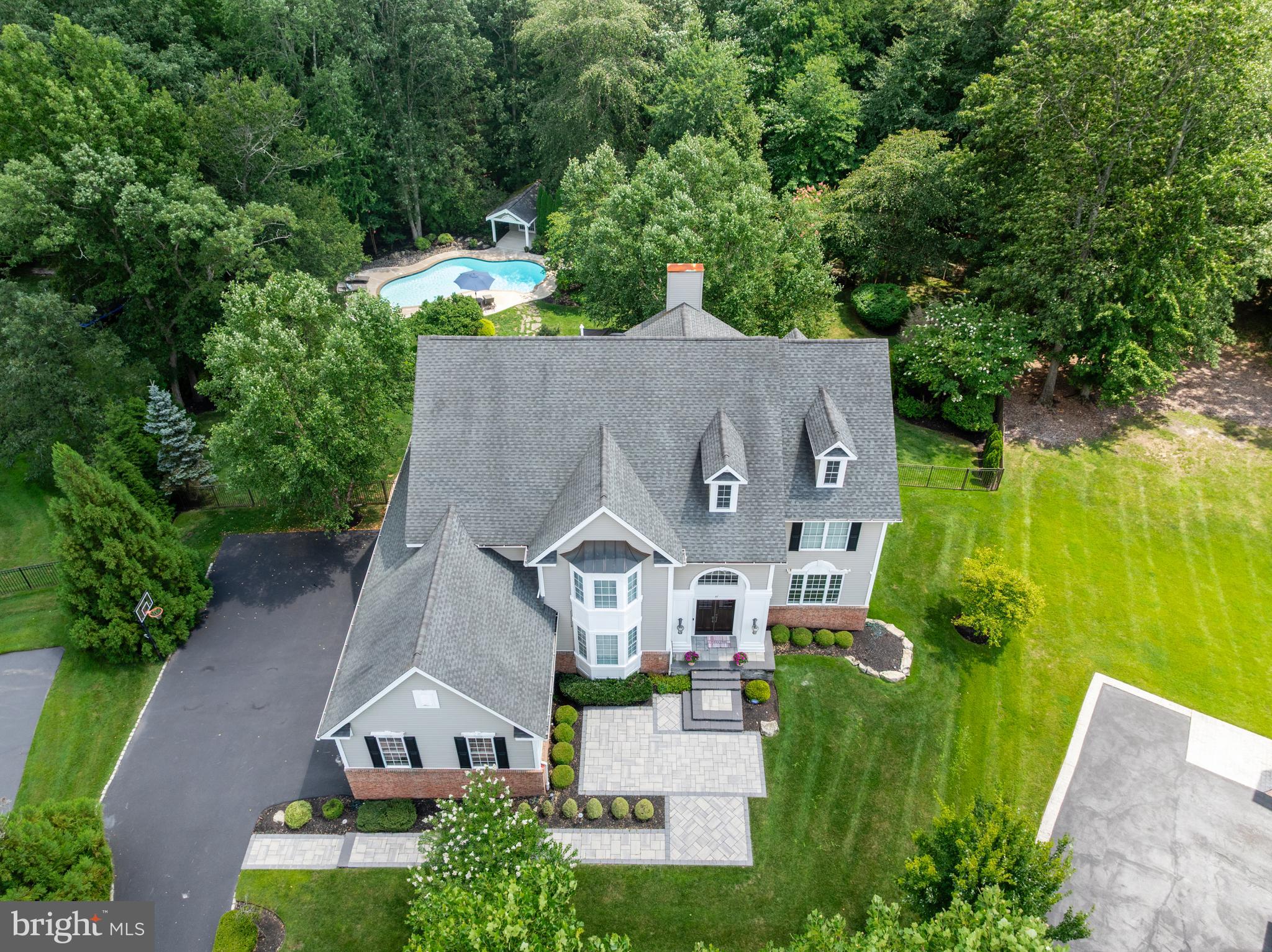 Welcome to 37 Foxcroft Way—an extraordinary executive residence where timeless sophistication, impeccable craftsmanship, and resort-style outdoor living come together in one of Mount Laurel's most prestigious neighborhoods, The Grande at Springville.From the moment you arrive, the stately curb appeal and beautifully manicured landscaping hint at the elegance that awaits inside. Step through the grand double doors into a breathtaking two-story foyer where soaring coffered cathedral ceilings, an impressive sweeping staircase with wrought iron balusters, and exquisite millwork immediately set the tone. Rich hardwood flooring extends throughout the entire first level, creating a seamless blend of warmth and sophistication.Designed for both elegant entertaining and comfortable everyday living, the formal dining room showcases stunning coffered ceilings, intricate moldings, and refined architectural details that elevate every gathering. Just beyond, the spectacular gourmet kitchen was thoughtfully expanded during construction and offers an abundance of custom cabinetry, granite countertops, a striking center island, stainless steel appliances (just two years young), tile backsplash, and generous prep space. The kitchen flows effortlessly into the dramatic two-story great room where walls of windows bathe the home in natural light while a floor-to-ceiling fireplace, beautifully reimagined with elegant quartz surround, serves as the stunning centerpiece of the home.Working from home has never been more inviting than in the private first-floor study, featuring brand-new plush carpeting and gorgeous custom wood built-ins that create an executive office worthy of the home's caliber.Upstairs, retreat to the luxurious primary suite, complete with spacious walk-in closets and a beautifully renovated spa-inspired ensuite bath that rivals today's finest luxury hotels. Every bathroom throughout the home has been beautifully updated with today's most desirable finishes, creating a fresh, cohesive, move-in-ready experience.The recently renovated walk-out lower level offers exceptional versatility with luxury vinyl plank flooring throughout, an updated full bath, guest quarters, game area, and expansive recreation spaces ideal for entertaining, multigenerational living, or extended overnight guests. Large egress windows and sliding glass doors flood the lower level with natural light, making it feel every bit as inviting as the main living spaces while providing seamless access to the backyard.Step outside and prepare to fall in love.Perfectly designed for entertaining on every scale, the backyard is truly a private resort. Enjoy morning coffee beneath the covered pavilion just off the kitchen, complete with ceiling fan and TV hookup, or host unforgettable summer gatherings on the expansive stamped concrete patio and grilling area below. The heated saltwater gunite pool becomes the centerpiece of this incredible outdoor retreat, while the pool house—with its own refrigerator and freezer—adds convenience for endless days spent poolside.Perhaps the home's most treasured feature is what lies beyond the backyard—a picturesque backdrop of permanently protected woodlands that ensures exceptional privacy and tranquil views for years to come.Meticulously maintained and thoughtfully updated throughout, recent improvements include two new HVAC systems (2026), renovated bathrooms (2026), luxury vinyl plank flooring in the lower level (2026), new carpeting in the office, staircase, and three bedrooms (2026), washing machine (2026), kitchen appliances (approximately two years old), and a freshly sealed driveway (2025).Sophisticated, impeccably maintained, and designed with both luxury and livability in mind, 37 Foxcroft Way is a rare opportunity to own one of Mount Laurel's finest executive homes—where every detail has already been perfected and all that's left to do is move in and enjoy.