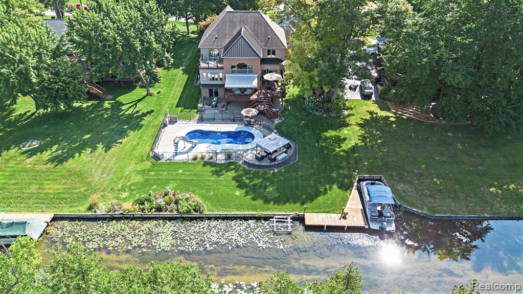Perfectly positioned in the highly desirable Waterford Hill community, this custom, impeccably maintained lakefront home on private, all-sports Greens Lake delivers refined luxury living with exceptional indoor-outdoor amenities. Set on a beautifully landscaped 0.54-acre lot surrounded by mature trees, this residence offers rare privacy, panoramic water views, and a true resort-style lifestyle—complete with a saltwater pool. Inside, a bright, open-concept floor plan is enhanced by gleaming hardwood floors, custom Pella windows, and soaring two-story ceilings that flood the home with natural light. A cozy fireplace anchors the main living space while showcasing uninterrupted lake views. The chef-inspired kitchen features quality cabinetry, quartz countertops, a custom island, and a breakfast nook with sliding doors to expansive lakeside decking—ideal for entertaining. A main-floor library/home office provides a perfect remote-work solution, complemented by a convenient laundry room. Upstairs, the luxurious primary suite offers a private balcony overlooking the lake, generous closet space, and a spa-style ensuite with dual vanities, jetted tub, and separate shower. Two additional bedrooms—including one with a walk-in closet—a full bath, and an airy loft complete the upper level. The finished walkout lower level adds over 1,800 square feet of living space, featuring high ceilings, a fireplace, full bath, and abundant storage—ideal for guests, recreation, or extended living. Outdoors, discover a true entertainer’s paradise with a sparkling pool, BBQ area with wet bar, third fireplace, and breathtaking lake views. Additional highlights include a heated 3.5-car garage with epoxy floors, extensive parking, access to Van Norman and Lester Lakes, and adjacency to serene Bay Court Park for unmatched privacy and natural beauty. Clarkston Schools via school of choice. Lovely gardens featured on the 2018 Garden Walk. Live the lake life without compromise. Recent appraisal at $1.344M available for review. IDRBNG