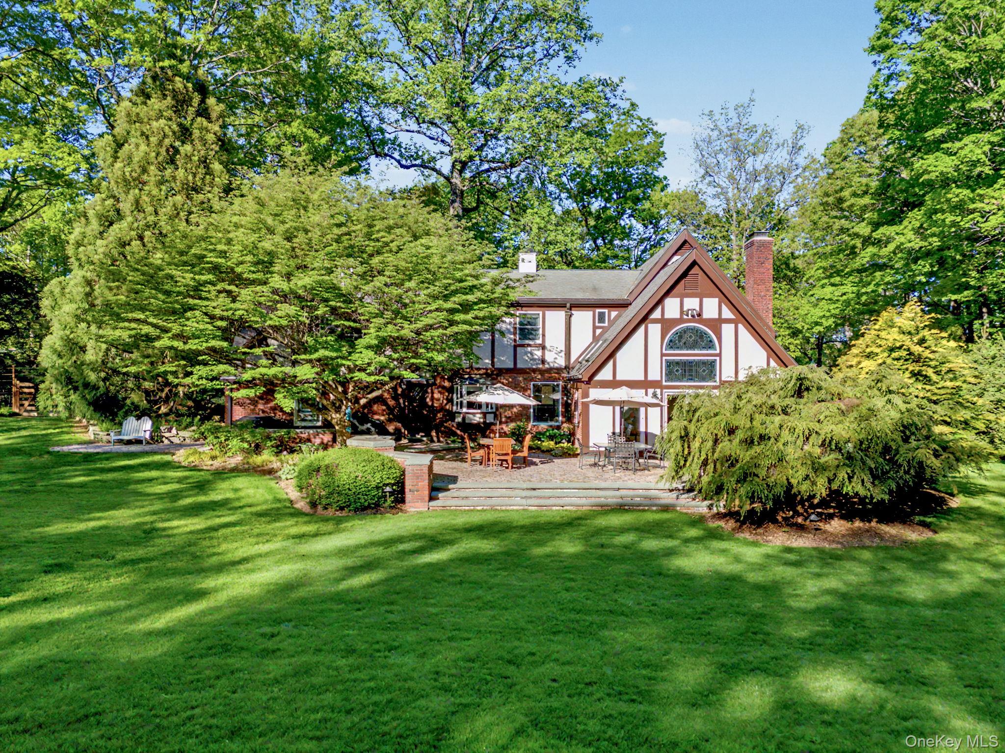First time on the market from the original owner, 80 Hack Green Road is privately set on almost three impeccably landscaped and flat acres between Scotts Corner and New Canaan. This distinguished brick and stucco colonial Tudor offers approximately 4,000 square feet of exceptional craftsmanship and timeless architectural character. Built by a professional contractor well beyond standard specifications, the home reflects enduring quality and meticulous updates throughout.A grand semicircular driveway welcomes guests with ample parking for up to twenty cars, creating a gracious arrival for grand-scale entertaining. Inside, thirteen custom-stained-glass windows infuse the interiors with remarkable artistry and warmth. The heart of the home features a sunlit eat-in kitchen perfectly positioned between the mudroom and the expansive great room with a 16-foot-high ceiling, which boasts dramatic skylights and a custom wet bar that opens seamlessly to the outdoor patio. A wood-paneled home office with built-in bookcases offers a quiet retreat overlooking the gardens, while a cozy recreation room features a high-efficiency cast-iron wood-burning fireplace. A whole-house central audio system effortlessly serves the main living spaces, making it highly functional for both vibrant social gatherings and quiet everyday living.The residence offers four bedrooms (originally 5) and three-and-a-half beautifully updated bathrooms. A vaulted upper-level bonus room, originally designed as a fifth bedroom, offers exceptional versatility as a playroom, creative studio, or guest suite. The finished lower level adds flexible square footage, featuring designated recreation and media areas perfect for a home gym or secondary entertaining space.The extraordinary bucolic grounds, cultivated over decades, with rare trees, including Japanese maples, weeping evergreens, Atlas cedar, and Japanese umbrella pine, feature an expansive, level lawn that is an absolute rarity in the area and ideal for grand-scale recreation. A standout feature is the rare pink granite cobblestone patio, masterfully crafted by Italian masons, which overlooks a tranquil fishpond accented by twin waterfalls. This outdoor oasis is completed by a playhouse, professional-grade swing set, and a half-court basketball area, all enveloped in absolute privacy. Ideally located just minutes from New Canaan, Grace Farms, several preserves and parks, Scotts Corners and Pound Ridge towns, St. Luke’s School, and the New Canaan train station, this property offers a peaceful retreat within the Bedford Central School District. Timeless. Refined. Exceptional.