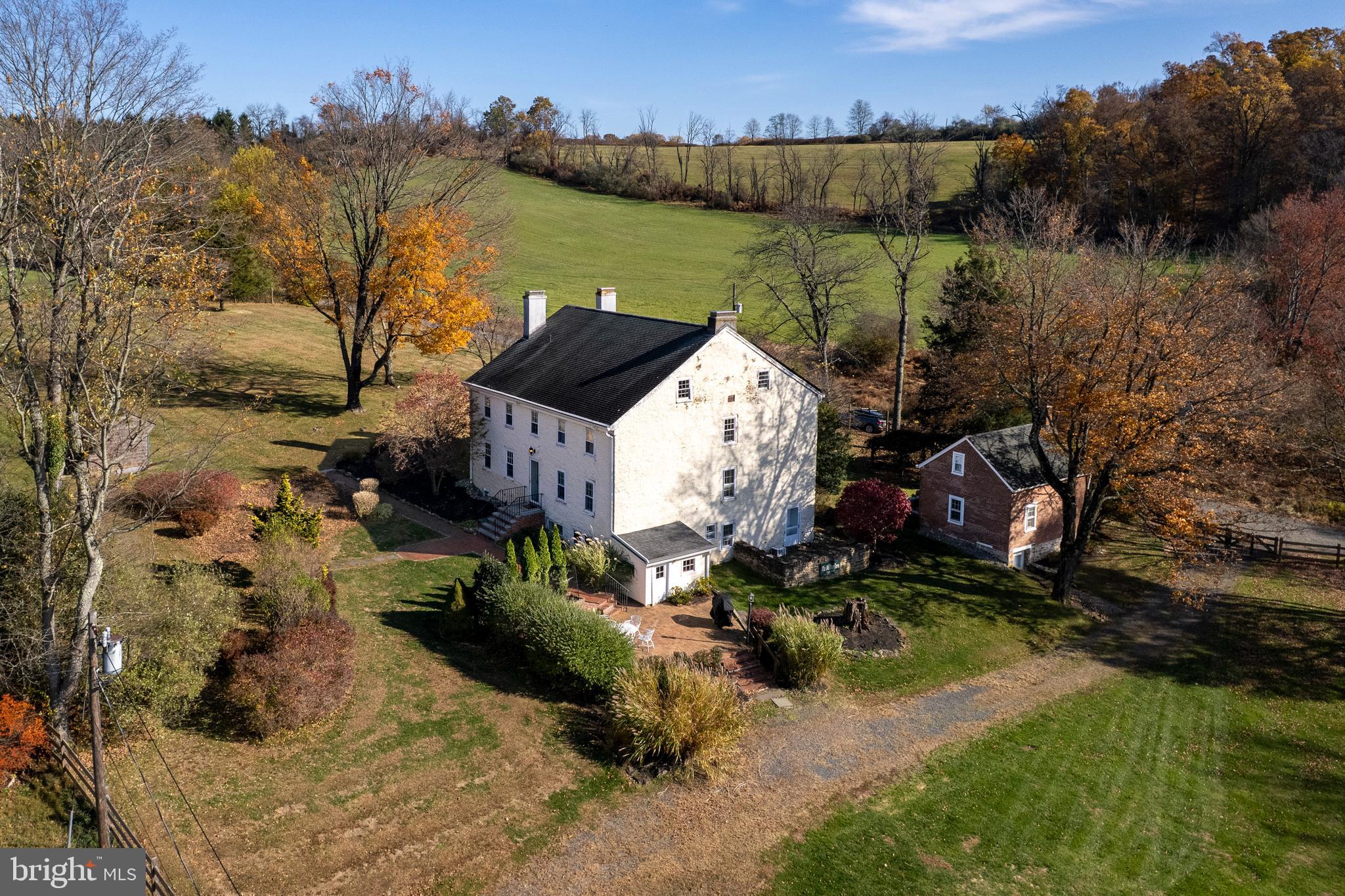 Driving along a winding country road in Hopewell Township, where farms, fields, and woodlands shape the landscape, a gazebo and romantic pond glint through the trees before revealing this stately 1840s historic home with a charming guest cottage. Brick patios and walkways weave through the gardens, connecting the house and cottage in a series of inviting outdoor spaces. The scene is quintessential Hopewell Valley: historic, peaceful, and surrounded by bucolic countryside. Inside, the main house retains the craftsmanship and character of the 19th century. Random-width wood floors glow with age and patina, while generously proportioned rooms are detailed with original doors and hardware, and window sills nearly a foot deep. A wide foyer welcomes visitors from the front entrance. The kitchen, anchored by a fireplace, sits oppositethe dining room, creating a natural gathering hub. Down the hall, a study with built-in bookcases offers a quiet retreat, while the living room features its own fireplace flanked by built-in shelving. Two deep storage closets and a half bath sit conveniently near the kitchen. Upstairs, three bedrooms share a hall bath, while a fourth bedroom has its own private bath. Closets, both in the bedrooms and along the hallway, provide storage uncommon in homes of this vintage. A walk-up attic offers additional potential, and the walk-out basement houses a laundry room, a gym, and a half bath. The guest cottage adds flexibility to the property. With its own kitchen and bath, it makes an ideal space for long-term visitors or even a creative studio. This offering carries a remarkable piece of local history. In the 19th century, it served as the Pennington area’s poor farm, part of a municipal system that provided housing and work for residents who had fallen on hard times. Established in 1843, it operated for more than a century, reflecting an early form of community social support long before modern public assistance programs. Today, the property’s peaceful setting tells an entirely different story. Located in the highly regarded Hopewell Valley School District and roughly midway between New York City and Philadelphia, it offers easy access to vibrant dining, shopping, culture, and mass transit. With its layered history, classic architecture, and idyllic surroundings, this home stands as both a reminder of Hopewell’s past and a serene country retreat for modern life!