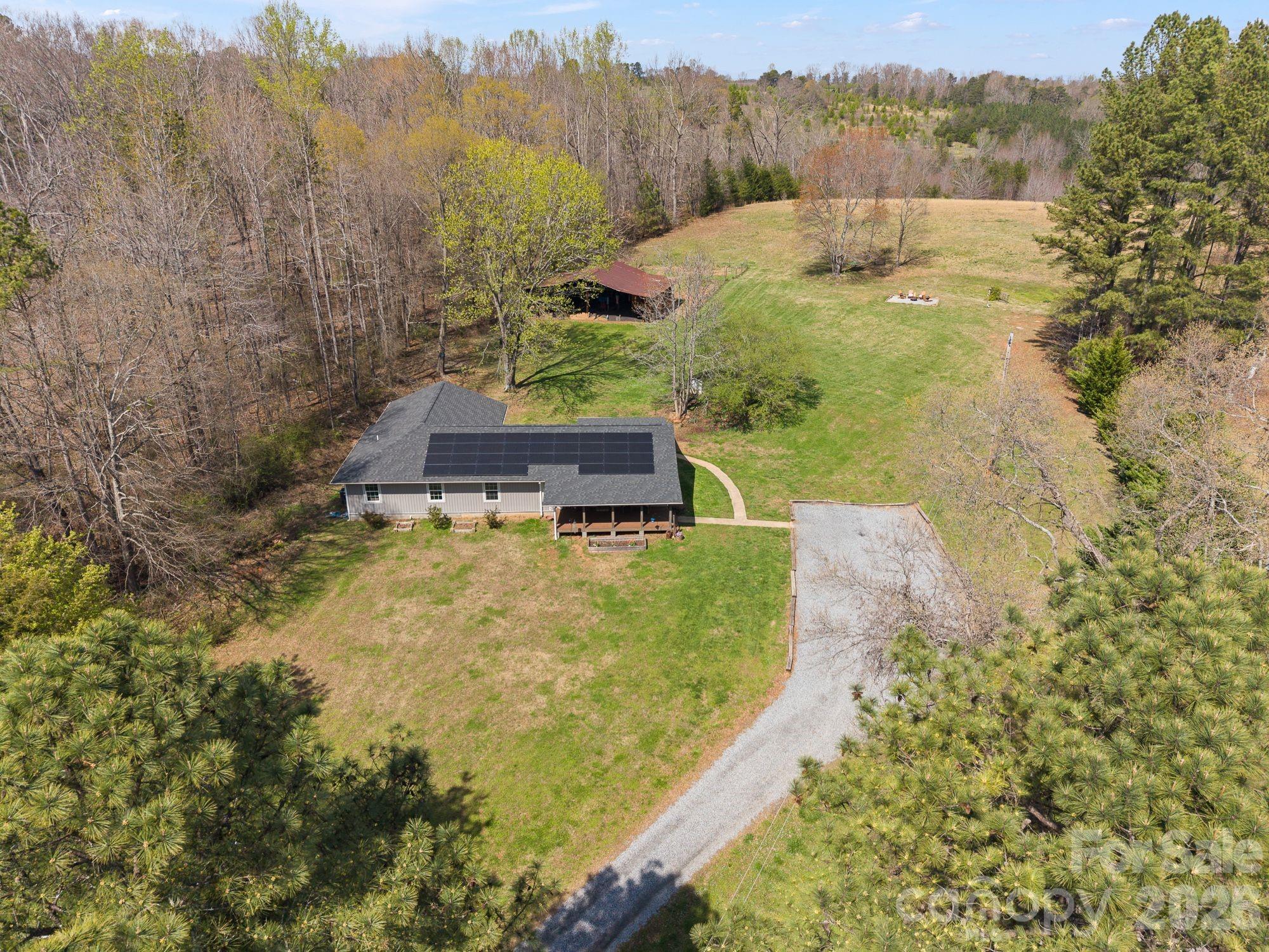 Set on over six picturesque acres, this beautifully reimagined single-level home offers the perfect blend of modern comfort and pastoral beauty. Originally built in 1987 and thoughtfully expanded and fully renovated in 2023—with an additional 1,100 square feet added—this property lives like new while retaining the warmth of an established setting.Inside, the expansive great room welcomes you with an open, airy feel—ideal for both everyday living and entertaining. The heart of the home is the stunning kitchen, anchored by an impressive 8-foot island, creating a natural gathering space for family and guests alike.The flexible floor plan features five bedrooms and four baths, including two private ensuite retreats—offering both comfort and versatility for multi-generational living or hosting.Step outside and experience the true magic of this property. Approximately three acres are cleared and ready for pasture, a riding ring, or other outdoor pursuits, while an additional acre of preserved woodland showcases rare native flora,  Evenings are best spent by the firepit under a canopy of stars—free from city lights and perfect for stargazing.Equestrian and hobby enthusiasts will appreciate the well-equipped 1,200-square-foot pole barn, complete with electricity, water access, a 30-amp plug, and a large walk-in chicken coop and run.Enjoy the outdoors year-round from the spacious front and rear porches, both finished with low-maintenance TREX decking and surrounded by established landscaping featuring hydrangea, hosta, iris, lily, dahlia, wisteria, and jasmine.Ideally located just 2.3 miles from the renowned Tryon International Equestrian Center.  See Features List for many more details of what this captivating property offers.