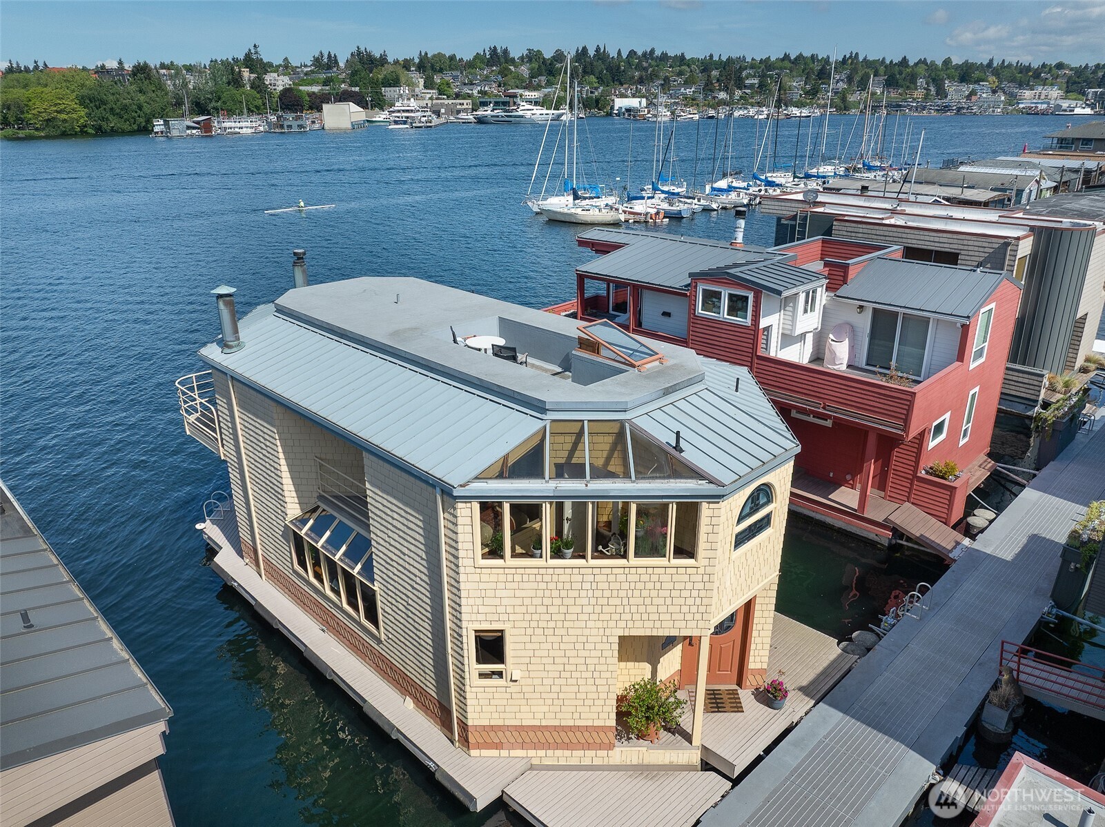 Perfectly positioned west-facing, coveted front-row Lake Union floating home with moorage, exceptional 3-bedroom + office, 2.25-bath offering sun-drenched, unobstructed panoramic views of the water, city skyline, and mountains, framed by expansive windows. The open-concept layout flows effortlessly from the inviting living spaces to the waterside decks, creating the perfect setting for entertaining, relaxing, or launching your next water adventure right from your doorstep.The kitchen features clean lines, abundant cabinetry, and a seamless connection to the main living and dining areas, while curated design details—including a striking copper fireplace, warm wood finishes, and vaulted open-beam ceilings—add warmth and sophistication throughout, plus a versatile main floor office/den/storage room. Perched above the main living spaces, the primary suite offers dramatic vaulted ceilings, expansive views, and dual private balconies featuring a spa-inspired bath, spacious walk-in closet, and built-in desk area. The upper level also includes two secondary bedrooms, 3/4 bath, laundry, a sun-filled garden nook, and access to the rooftop deck with exciting potential to create your dream entertaining space.  Dedicated 45'+ moorage slip, additional moorage for smaller boat, 1 garage parking space w/EV charger, storage, additional residence parking. Vibrant Eastlake neighborhood