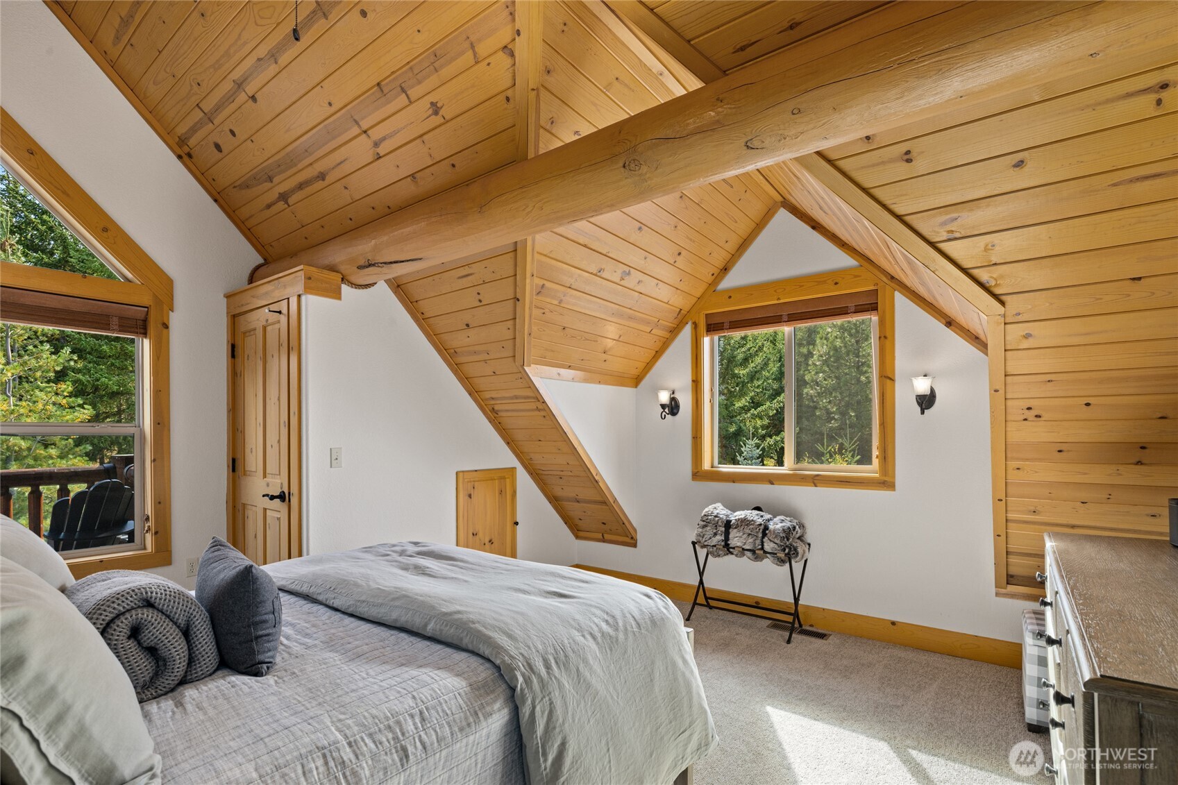 Another view of the guest bedroom highlights its vaulted architecture, warm wood detailing, and surrounding forest setting.