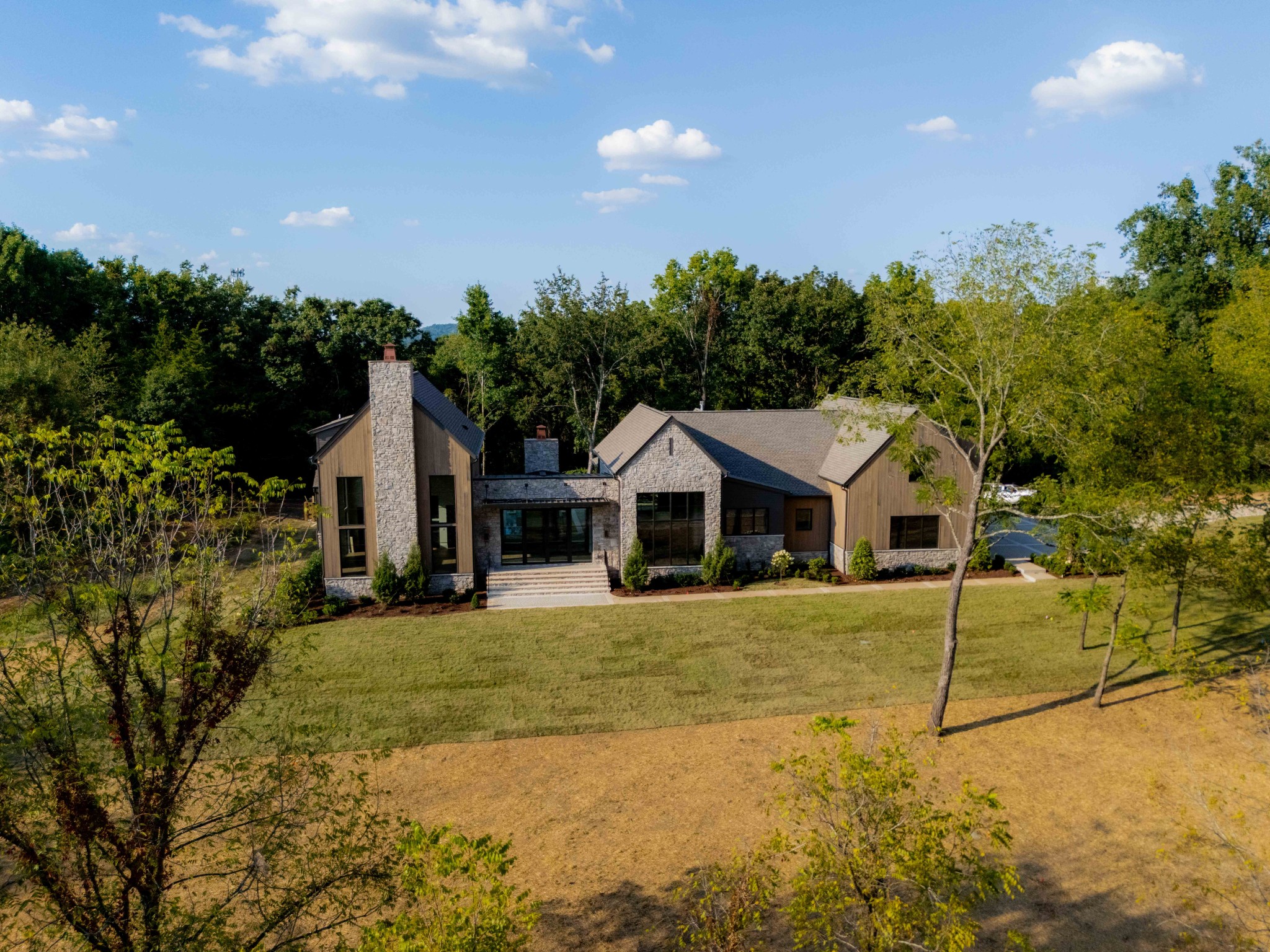 Gracefully set on 5.70 private acres in the premier Arrington Woods community, this exceptional custom home by Cadre Homes offers a rare blend of timeless design and modern luxury. With 5 bedrooms, 5 full and 2 half baths, and over 6,200 square feet, every detail has been thoughtfully curated for elevated living. A striking exterior of stone, Hardie plank siding, and metal roof accents creates a lasting first impression, while expansive windows fill the home with natural light. Inside, wide-plank European white oak flooring, custom millwork, and designer finishes establish a refined yet welcoming atmosphere. The chef’s kitchen is a true centerpiece, featuring a 48” Wolf range, 60” paneled refrigerator/freezer, built-in microwave, coffee system, and paneled dishwasher. Custom inset cabinetry and quartz countertops provide both beauty and function, ideal for everyday living and entertaining. The main-level primary suite is a private retreat, complete with a spa-inspired bath offering a freestanding soaking tub, oversized tile shower with dual shower heads, heated floors, and custom walk-in closet systems. Additional living spaces include a spacious bonus room prewired for surround sound and flexible areas for gathering or relaxation. Outdoor living is equally impressive, with covered porches finished in tongue-and-groove wood ceilings overlooking the scenic acreage. The home also features a 3-car garage with EV charging capability, tankless water heater, smart home prewiring, and energy-efficient systems throughout. Professionally designed landscaping and irrigation enhance the natural beauty of the property. Estimated completion is October 1st, with the pool anticipated to be completed approximately four weeks thereafter. This is a rare opportunity to own a thoughtfully designed luxury estate in one of Arrington’s most sought-after communities.