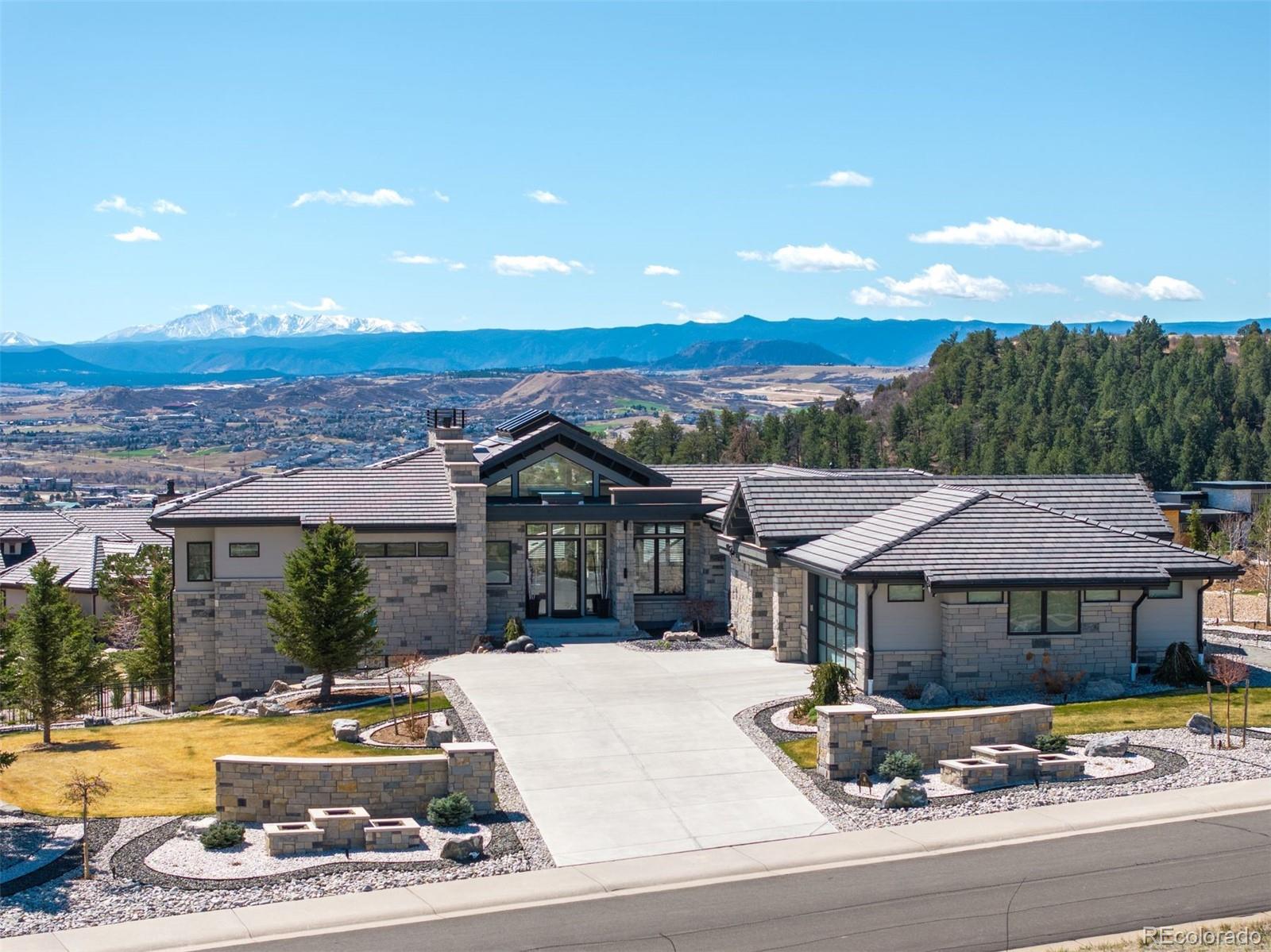 Positioned on an elevated corner lot, this spectacular modern ranch has it all! Pikes Peak views from every room, a saltwater infinity pool and spa, resort-style outdoor living, and main-level living in a home that looks and feels brand new. The expansive covered deck is an entertainer's dream, offering front-row views of the sunrise, sunset, and summer fireworks over the town of Castle Rock, all framed by the mountains. With low-maintenance xeriscape grounds that bloom continuously from spring through fall, this is Colorado living at its finest. Inside, the great room is highlighted by 20-foot vaulted ceilings, a custom ridge skylight that opens for a breeze, and a wall of windows that frame Pikes Peak. The linear fireplace with Italian marble surround anchors the space, while the open flow carries seamlessly into the kitchen, appointed with Dacor and Sharps appliances, double ovens, 36-inch refrigerator and freezer, and floor-to-ceiling white cabinetry. The main-level primary suite offers a true retreat with a fireplace, bathroom with freestanding soaking tub, multi-head walk-in shower, and a generous two-sided walk-in closet with custom organization system. The lower level expands the living experience with a recreation room, fireplace, wet bar, gym, and walkout access. Outside, the upper covered deck features an outdoor kitchen and unobstructed views in every direction. Below, the gated lower patio flows directly to the infinity pool, jet spa, and built-in fire pit, all surrounded by professionally designed landscaping, flagstone pathways, and programmable outdoor lighting. Every detail has been considered, from the automated smart home system controlling lighting, audio, security, and window coverings via mobile app, to the $20K+ wiring investment, whole-home surround sound, and resort-caliber pool technology. With over $700K in seller improvements, homes this exceptional, in this condition, and with these views, simply don't come along often.