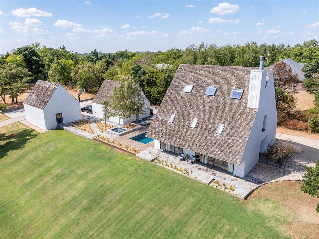 A rare architectural offering a Scandinavian inspired compound defined by dramatic steep pitched gables, crisp white vertical board siding, and cedar shake roofs punctuated with skylights. The clean, minimalist forms deep set windows, recessed entries, and sculptural chimney  give the home a striking, gallery-like presence that stands apart from anything else in the area.The main house offers five bedrooms and four full bathrooms across three levels, with light-filled living spaces that open through walls of glass to the grounds. Outside, a resort style pool and spa are wrapped in an expansive wood deck with a fire pit lounge  built for both quiet evenings and entertaining at scale.A two story, 1,100 sf guest house mirrors the main home's architecture, offering flexible space for extended family, guests, or a private studio. A detached garage adds an attic above plus a finished flex room with custom storage, ideal as a workshop or home gym.Set on two acres of manicured lawn framed by mature trees, the property functions as a private retreat just minutes from Edmond conveniences. Served by a private well with variable-pressure pump and water softening system.