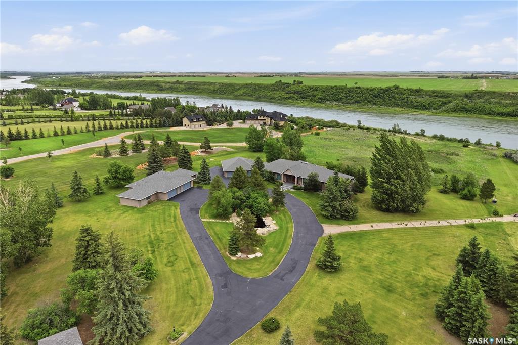 This 3640 sq ft Walkout Bungalow is situated on a 8.8 acre parcel with views of the South Saskatchewan River. With a wonderful location in an active community with rink & play center. Walking into this home, you are welcomed with double-door entry with phantom screens and a spacious foyer leading to an open floor plan with 10 ft ceilings. Great Room features a gas fireplace and custom Redl built-ins, large windows with scenic views. Custom Redl Kitchen is a perfect space with an abundance of cabinets, oversized island with seating, storage, gas cooktop, sink with garburator, granite countertops, baking counter with appliance storage, wall pantry with roll outs, Sub Zero Fridge, built in dishwasher, brand new trash compactor, built-in oven & microwave, coffee bar, dining nook with garden door to composite deck. Formal dining room with a buffet niche. Primary Bedroom is a full retreat with views of the river and access to the deck, gas fireplace with built-ins, dual walk-in closets(1 with stackable washer & dryer), a 4 piece en-suite with in-floor heat, air jet soaker tub, separate shower, dual vanity with granite top & linen closet, sitting area with direct access to basement gym and 3 piece bathroom. Den with a tray ceiling and bayed window.2-piece bathroom with custom stone countertop, laundry room with cabinets, sink, & craft/sewing desk complete the main. Walkout basement features in-floor heat, large family room with 3-way gas fireplace, garden door to covered, partially enclosed patio,games area with wet bar feature seating, fridge,dishwasher & sink. 2 large bedrooms with jack&jill 4- piece bathroom, den/craft room with closet, large mechanical/storage room with wine room. Home is wired for sound system,LED lighting up the driveway, new carpet(2023), new boiler(2023), central vac,4 furnaces & central air, window treatments, & generator for backup power. Attached 8-car heated garage, detached 12-car heated garage/workshop with hoist &cabinets &2-piece bathroom.