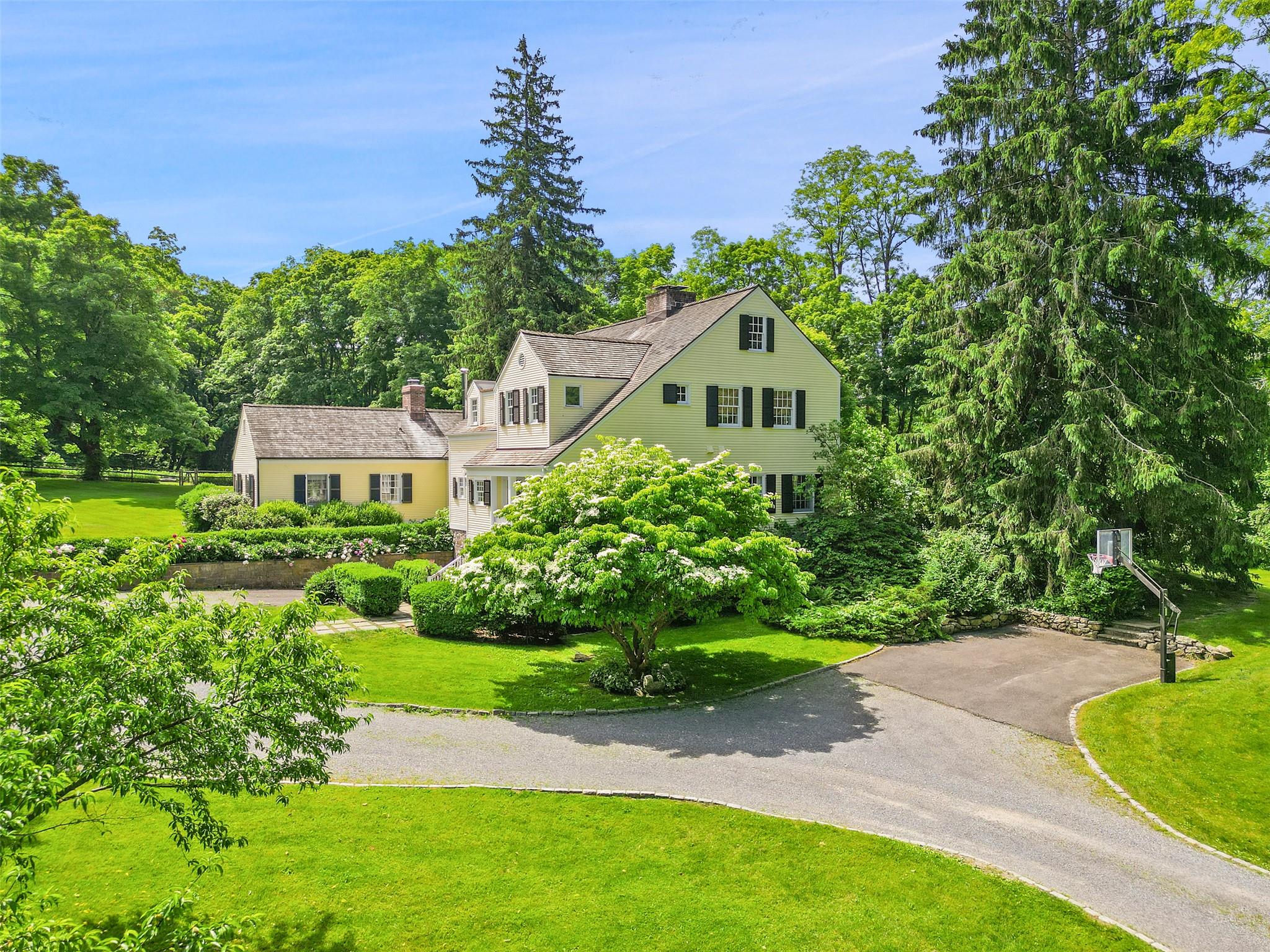 In a world of its own, situated on land that once grazed sheep, this stunning and sophisticated farmhouse welcomes its next devoted stewards. Abundant light shines through every room, warming the house and making it a home. Wonderfully private, yet just minutes from Bedford Village and Pound Ridge, the property offers easy access to the Mianus River Gorge and miles of scenic hiking trails. Inside you will find four comfortable, cheery bedrooms including a main-floor guest suite-perfect for visitors seeking privacy. A fifth, smaller room upstairs and adjacent to the master suite, can be used as an office, work out room or nursery. 
The layout is designed for both relaxed everyday living and elegant entertaining. Cozy up in the pine-paneled den with its own fireplace and lots of bookcases, or gather in the large living room beside the massive stone hearth on chilly evenings. The gracious, inviting dining room with corner cupboards, sets the stage for memory-making dinners, while the gourmet, spacious kitchen, complete with its own fireplace and ample seating space, is a favorite gathering spot year-round. 
In the warmer months, dine al fresco on the expansive terrace--a perfect place for parties or simply enjoying the sense of place surrounding you, including the stone-cased, heated pool, which also has another spot for dining, under a rose drenched pergola. The lower-walk-out level, with yet another fireplace, offers a versatile hangout haven for family and friends. This is a home that truly embraces all four seasons while offering you endless possibilities to savor the best of country living.
Throughout the property, delightful perennial gardens bloom from spring through fall, while a raised bed, vegetable, cutting flower and herb garden is just steps away from the kitchen door. Walk around the back yard, to find your very own English rose garden tucked into the terrace, also easily accessible through french doors in the den. And if you're wondering what to serve for dessert, try some of the fruit from the orchard which is planted in the style of a romantic walkway.
This is a once in a lifetime spot; the sort of place you hope to find, but rarely do!