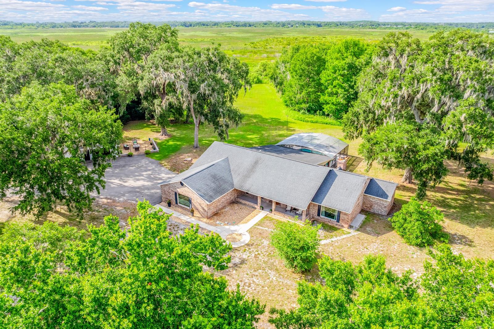 Virtually Staged. Seller may consider buyer concessions if made in an offer ~ Peaceful, private, and packed with possibilities, this beautifully updated POOL HOME sits on TWO PARCELS totaling 5 ACRES with a PRIVATE GATED ENTRANCE, a 3/4 ACRE POND WITH DOCK, and beautiful views of Lake Runnymede! Recent upgrades include a Rheem intelligent WATER HEATER (2026), Fleck AIO WATER FILTRATION/SOFTENING SYSTEM (2026), refreshed third bath (2026), updated laundry room (2026), painted pool deck and patio (2026), CEDAR TONGUE & GROOVE FRONT PORCH CEILING (2026), hurricane-impact DOUBLE PANE WINDOWS (2025), FRESH INTERIOR & EXTERIOR PAINT (2025), a beautifully remodeled primary bath (2025), and LUXURY VINYL PLANK FLOORING THROUGHOUT (2023/2026). The high-efficiency 5-ton, 18-SEER A/C was installed (2024), and the roof is approximately 7 years old. Designed for both everyday living and entertaining family and friends, the OPEN CONCEPT floor plan offers flexible spaces, including a BONUS ROOM/4TH BEDROOM with potential for an in-law suite and a FLEX/OFFICE that could easily become a 5th bedroom. The chef's GOURMET KITCHEN anchors the interior, paired with a light and bright living space that boasts a WOOD BURNING FIREPLACE built into a brick feature wall, while an OUTDOOR ELECTRIC FIREPLACE creates the perfect gathering space to relax and unwind. Be sure to explore the spacious PRIMARY SUITE, ideally situated on its own wing with a picture window that lets the light pour in, a huge UPGRADED EN-SUITE BATH that feels like stepping into a spa and the perfect complement of a large WALK-IN CLOSET complete with custom storage. The detached 32x42 GARAGE/WORKSHOP features 12-foot ceilings and AT&T Fiber, making it ideal for hobbies, storage, business use, or future expansion. Outside, enjoy total privacy with mature trees, sprawling green space, banana, guava, rose apple, elderberry, blackberry, avocado trees, and pineapple plants. With AT&T Fiber Internet, Starlink capability, NO HOA, seller financing available, and unlimited potential for large gatherings, recreation, or multi-generational living, this one-of-a-kind property feels worlds away while remaining just 20 minutes from Lake Nona and convenient to TOP-RATED SCHOOLS, shopping, dining, parks, major roadways, and Central Florida attractions. ** 5 ACRES ** PRIVATE POND ** LAKE VIEWS ** ENDLESS POSSIBILITIES ** Welcome to the lifestyle you have been searching for in St. Cloud ~ and WELCOME HOME!