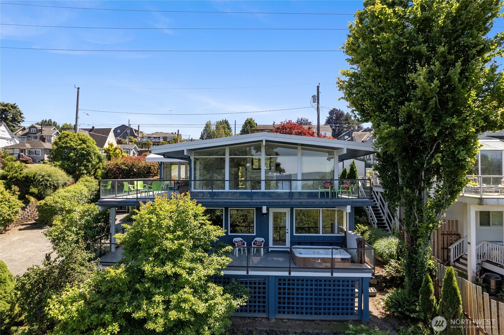 Perched above the treetops near Tacoma's beloved Proctor District, this architecturally stunning 1964 MCM home delivers the views, the light, and the lot that rarely come together at once. Floor-to-ceiling windows and soaring vaulted ceilings frame sweeping Puget Sound vistas and a lush, verdant treescape across every sightline. A gas fireplace anchors the main living area, while a wraparound two-level deck and private hot tub invite year-round outdoor living. Two main-floor bedrooms are bathed in natural light with access to a private garden, a freshly painted interior and exterior ensure move-in-ready appeal. The mature grounds — Hawthorn, apple trees, and established plantings throughout — offer privacy and seasonal beauty on a rare 12,300 SF lot with possible subdivide potential, an extraordinary opportunity for investors or buyers seeking long-term land value. A separately accessed lower level complete with kitchen, bedroom, and bath functions beautifully as an income-producing ADU or multi-generational suite — flexibility built right into the footprint. Homes with this combination of architectural integrity, Sound views, income potential, and subdividable land don't surface often. This one is worth a serious look.