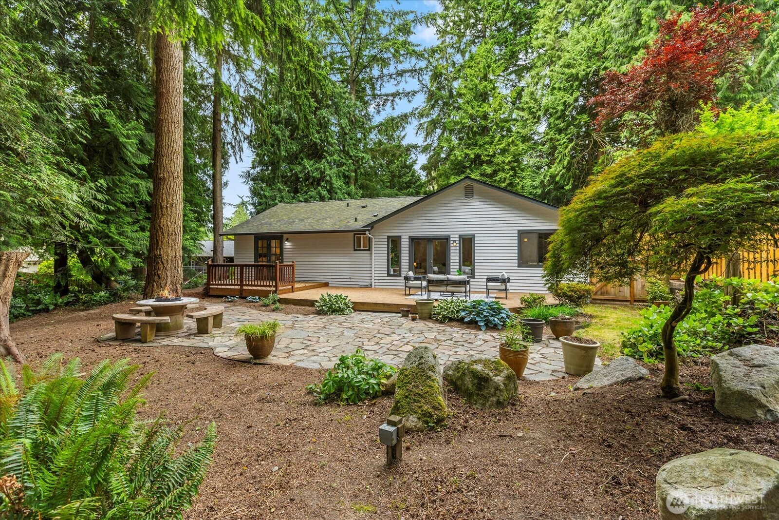 Tucked beneath the trees like a well-kept secret, sits single story serenity. A modern escape wrapped in nature this home delivers sensible living with smart updates and effortless style. Fresh interior paint and a well-maintained layout mean all the hard work is done. A thoughtful floor plan flows easily from room to room, with the private primary suite offering French doors that lead straight to your private PNW playground. Step outside to an expansive wood deck perfect for hosting friends or enjoying quiet mornings. Towering evergreens and lush landscaping create a calm, forested backdrop just minutes from city life.  Follow the stone path to a built-in seating nook-ideal for cozy fires or your morning coffee ritual.