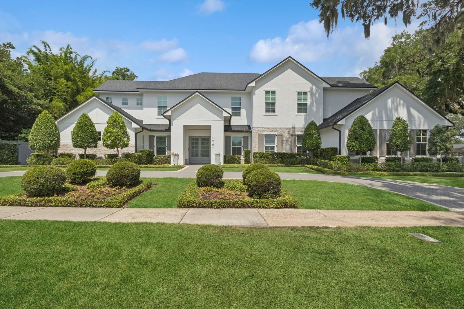 One of the most coveted neighborhoods in all of Winter Park! This custom-built 5-bedroom, 5.5-bath residence was completed in 2017 and first sold in 2018. Lovingly maintained by the original owner and elevated with high-end designer finishes, the home showcases the impeccable vision of renowned designer Ted Maines, who reimagined much of the interior with timeless sophistication. Perfectly positioned on a prime over-sized corner lot, the home blends transitional architecture with modern elegance. Sunlight fills the open layout through expansive sliding doors, creating effortless indoor-outdoor flow. The main living area seamlessly connects a formal living room and spacious dining area to the gourmet kitchen, complete with custom cabinetry, Carrara marble surfaces, and Sub-Zero and Wolf appliances. A cozy family room with fireplace provides a relaxed yet stylish gathering space. The private downstairs primary suite opens directly to the lanai, saltwater pool and features a spa-style bath. A secondary ground floor bedroom is perfect for guests or multigenerational living. Upstairs, enjoy a spacious loft with custom bar, leading to a versatile media room. Three additional en-suite bedrooms complete the second level. Recent enhancements include a full-house generator, a newly added semi-circular driveway that enhances curb appeal and functionality, and three newer A/C units with re-engineered, high-efficiency ductwork to ensure optimal climate control throughout the home. The outdoor living space is equally impressive, offering a saltwater heated pool and spa with cascading waterfall, elegant stone decking, ambient lighting, and a covered summer kitchen—ideal for year-round entertaining. A rare 3-car garage completes this exceptional home. All just moments from the shops, dining, and charm of downtown Winter Park.