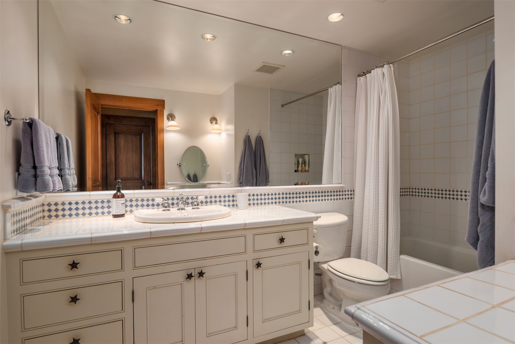 Bathroom with tile countertop, tub/shower combo, and star-accented cabinetry