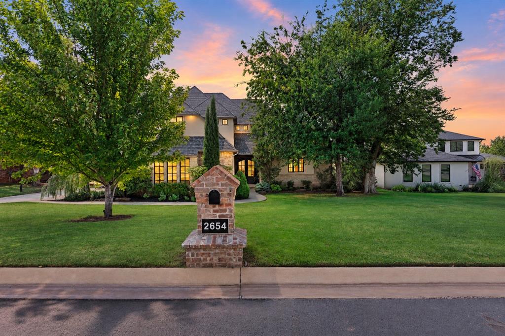 Welcome to 2654 Loblolly Lane, an exceptional luxury residence in the gated Summit Lake Estates community of Deer Creek. Perfectly positioned along the community pond, this remarkable home pairs refined interiors with unforgettable Oklahoma sunsets. A grand double-door entry, welcomes you into an impressive great room where custom ceiling beams, a brick-hearth fireplace with shiplap detailing, and walls of windows frame the peaceful pond beyond. The adjoining dining area transitions beautifully from casual gatherings to more elegant occasions while maintaining an effortless connection to the kitchen and living spaces. Designed for entertaining, the kitchen showcases an enormous center island with generous seating, double ovens, abundant workspace, and a spacious pantry. Barn doors open to a private study with a dramatic vaulted ceiling, creating an inspiring place to work from home. The primary suite is a private sanctuary featuring a spa-inspired bath with two separate vanities, an oversized walk-in shower, and a dreamy, beautifully designed closet with custom organization, abundant storage, and a boutique-inspired feel that makes getting ready each day feel like a luxury. The utility room connects directly to the primary closet for added convenience. A private downstairs ensuite provides luxurious accommodations for guests, while a powder bath and mud bench add thoughtful functionality. Upstairs, three additional bedrooms are complemented by a spacious bonus/game room with a built-in desk. Outside, the covered patio and outdoor fireplace create a spectacular setting to unwind. Additional features include a private water well and aerobic septic system. Luxury, privacy, and extraordinary views come together beautifully at 2654 Loblolly Lane. Welcome Home!