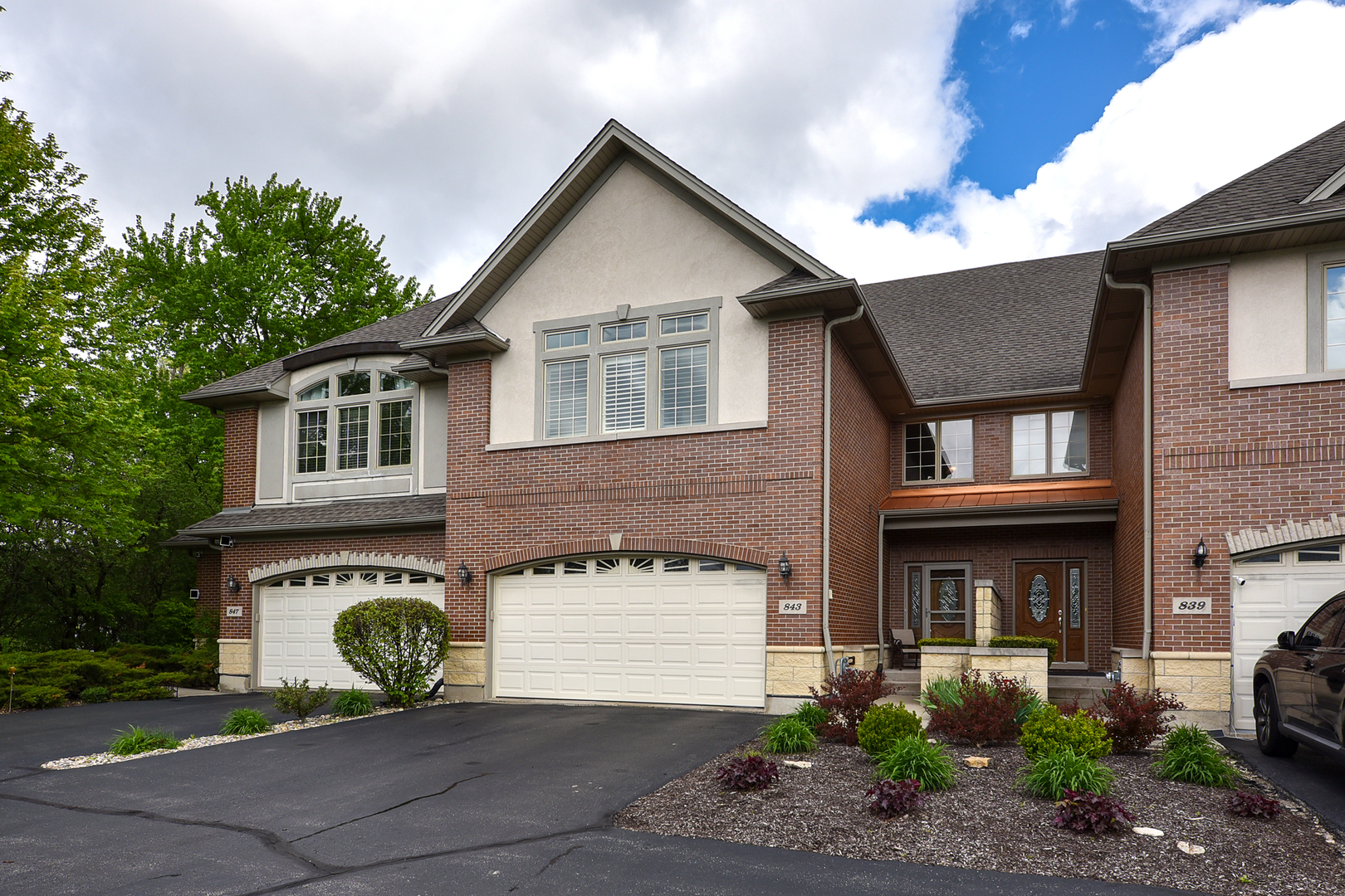 An exceptional newer townhome showcasing an elegant stone and brick exterior with undeniable curb appeal and presence. From the moment you arrive, the quality and craftsmanship is immediately evident. A welcoming two-story foyer sets the tone, highlighted by a striking split staircase that makes a refined architectural statement. Beyond, the dramatic two-story great room is anchored by rich hardwood flooring that flows seamlessly throughout the main level, while a gas fireplace creates a warm and inviting gathering space. The formal dining area offers both sophistication and versatility, perfectly suited for intimate dinners or larger, more elegant entertaining. A sliding door provides access to a private patio and yard beyond, enhancing the home's natural flow. The adjacent oversized kitchen is thoughtfully designed with an abundance of cabinetry and expansive stone countertops, offering both beauty and functionality. The main level is further complemented by 9-foot ceilings, a stylish powder room, and an oversized mudroom conveniently located off the garage. Upstairs, the primary suite serves as a true retreat, featuring a tray ceiling, transom windows, two walk-in closets, and a luxurious en-suite bath. A generously sized second bedroom, an additional full bath, and a dedicated laundry room complete the upper level. The finished lower level continues to impress with a beautifully designed recreation space, ideal for a home theater, game day gatherings, or relaxed everyday living. A convenient half bath adds to the functionality. Additional premium features set this home apart, including zoned heating and cooling, epoxy-coated garage floors, plantation shutters, and more. Meticulously maintained and reflecting true pride of ownership throughout, this is an exceptional opportunity not to be missed.