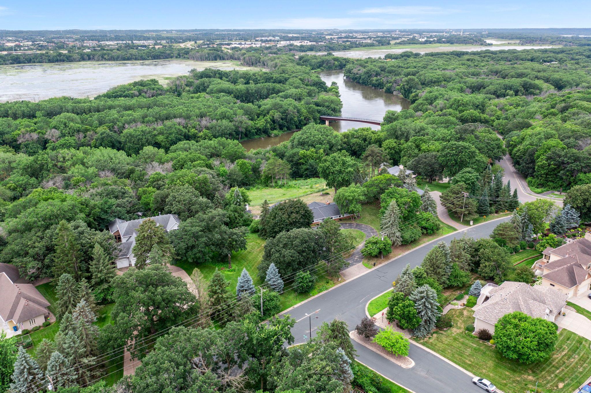 Set atop river bluffs on a stunning 2-acre lot, this one-level rambler offers privacy, space, and panoramic views of the Minnesota River Valley. Nestled next to a serene Wildlife Preserve, it seamlessly blends nature and comfort. The open-concept layout features light-filled living spaces, a well-equipped kitchen with ample cabinetry and dining area, and a sunlit living room with bluff views, gas fireplace, and custom built-ins. A dramatic family room boasts 15-ft vaulted ceilings, walls of windows, and walk-out access to the backyard. The spacious primary suite is a private retreat with ensuite bath, generous closet space, and breathtaking views. A second ensuite bedroom is perfect for guests, while two additional bedrooms and two more baths provide flexibility. Additional highlights include a large laundry room, finished 3-car garage with epoxy floors, two outdoor sheds, and a fully fenced backyard. Steps from the Minnesota Valley State Trails and minutes from Hwy 169, shopping, and dining—this rare gem offers daily sunrise and sunset views 365 days a year and endless wildlife.