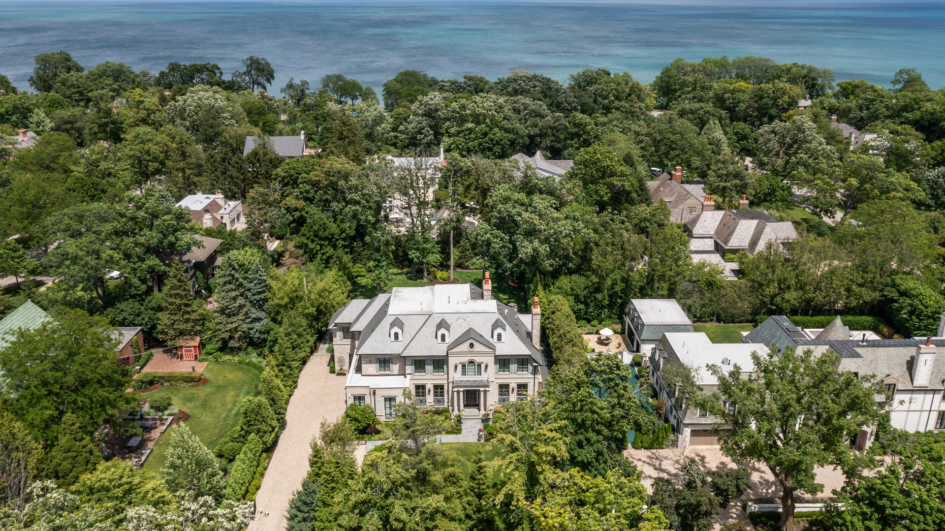 One of the North Shore's most prestigious addresses, 677 Sheridan Road, is a magnificent estate that seamlessly blends timeless architectural elegance with modern luxury living. Situated just two blocks from Lake Michigan, Glencoe Beach, downtown Glencoe, the Metra Station, and Writer's Theatre, this residence offers an unparalleled lifestyle in an enviable location. First occupied in 2020, there is over 10,000 sq ft of exquisite living space.  The home sits on a .65-acre wooded lot with 108' of frontage on Sheridan Road and impressive lot depth of 260'. Mature trees, lush gardens, and professionally curated landscaping create a private sanctuary that feels worlds away, yet minutes from every convenience. From the moment you arrive through the custom security gate and stately stone pillars, the exceptional craftsmanship becomes apparent. The stone exterior with brick paver drive is complemented by a true slate roof, copper gutters, bluestone terraces, and meticulously maintained grounds. The grand-scale interior features 10.8' ceilings, rich millwork, and elegant French doors. Recent enhancements have transformed the grounds into a private resort-like retreat. Extensive landscaping and hardscaping are complemented by irrigated lawns and gardens, a massive outdoor fireplace, a bocce court, and an outdoor kitchen featuring a 48-inch DCS grill, Sub-Zero refrigeration, and an authentic Chicago Brick Pizza Oven. Programmable architectural lighting illuminates the grounds and majestic white oak tree canopy, creating breathtaking evening ambiance. Inside, every room reflects a refined design aesthetic. Recent interior renovations by Jen Marie Interiors introduced a sophisticated layer of luxury. The great room showcases illuminated shelving and custom cabinetry, a striking limestone fireplace, Phillip Jeffries ceiling treatments, and elegant new lighting. The dining and living rooms have Holly Hunt window treatments, Phillip Jeffries wallpaper, statement chandeliers, custom-painted millwork, and gorgeous ceilings. The dramatic foyer with floating staircase has been transformed with custom wall moldings, redesigned staircase spindles, and a 15' hanging Ochre chandelier with over 40 crystal LED drops. This bespoke design elicits a jaw-dropping first impression. The gourmet kitchen was thoughtfully tailored to accommodate both everyday living and large-scale entertaining. Anchored by a designer Italian range, mirrored Sub-Zero refrigeration, dual Viking dishwashers, a Shaws farmhouse sink, and an integrated espresso and cappuccino station, the space is as functional as it is beautiful. Striking Iceberg quartzite countertops, an oversized center island, an intricate tile backsplash, and elegant Carrara marble flooring create a timeless and sophisticated aesthetic. Adjacent gathering spaces flow effortlessly to the outdoor living areas. The handsome walnut-paneled library is a quiet place to work; it opens to the all-season porch with new operable insulated windows. There are 6 spacious en suite bedrooms, and 7.2 baths, each appointed with heated floors and custom-designed vanities. The luxurious primary suite has a beautiful fireplace, two generous custom walk-in closets, and a marble bathroom with two vanities, steam shower and soaking tub.  The lower-level rivals the finest of private clubs with its temperature-controlled wine cellar with glass doors, custom wet bar, family room with fireplace, billiards area, private guest suite, professional theater, and fitness center complete with sauna. A full-size sport court provides year-round recreation and includes a golf simulator. Additional amenities include a central vacuum system, whole-house generator, smart home technology, LED lighting, advanced foam insulation, and 4-car garage with coated flooring and 4 thermostat-controlled heaters.  Rarely does a home offer this level of comfort, sophistication, craftsmanship, and recent investment. This is truly one of the North Shore's finest!