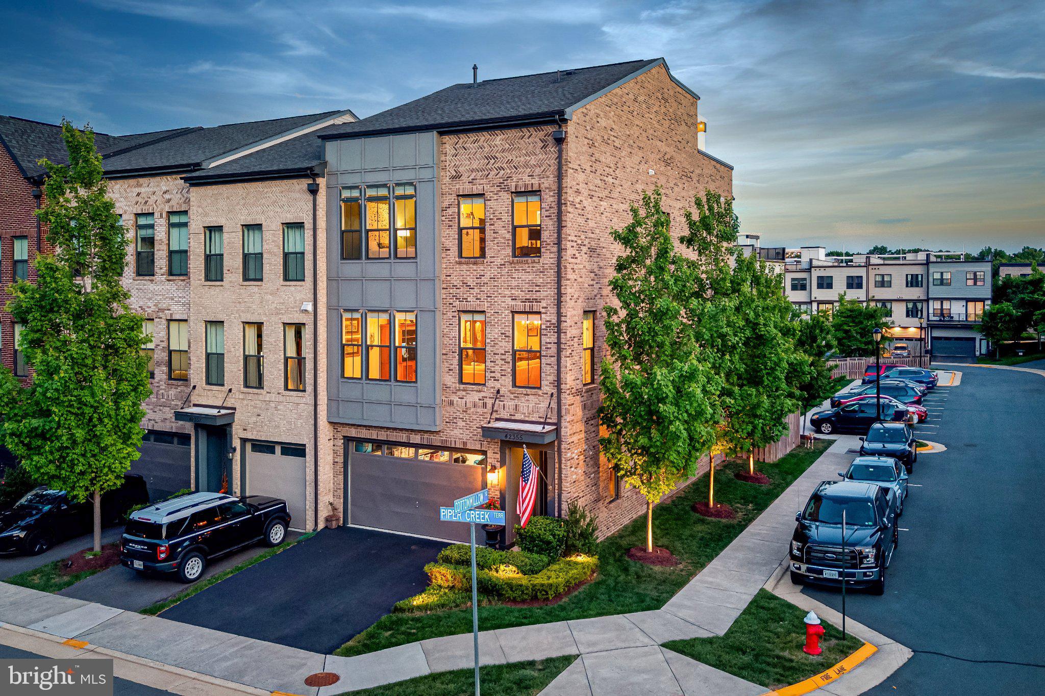 Discover a luxurious lifestyle in this exquisite end-of-row townhouse nestled in the vibrant Brambleton Town Center. This contemporary Craftsman-style home boasts an impeccable blend of elegance and comfort, featuring four spacious bedrooms and three and a half beautifully appointed bathrooms. Step inside to find an open floor plan that seamlessly connects the gourmet kitchen, complete with stainless steel appliances, upgraded countertops, and a generous island, to the inviting dining and living areas. The home is adorned with wide plank engineered hardwood and ceramic tile, complemented by plush carpeting in the bedrooms. Enjoy the convenience of a walkout basement with ample natural light, perfect for entertaining or relaxation. Outside, the corner lot offers a beautifully landscaped rear yard that backs to serene trees, providing a tranquil escape. The extensive hardscape and multiple outdoor spaces, including a roof deck and patio, are ideal for gatherings or quiet evenings under the stars. Community amenities enhance the exclusive lifestyle, featuring multiple pools, clubhouses, and various recreational facilities, including basketball courts and bike trails. With high-speed internet, grass cutting and cable included in the association fee, modern living is at your fingertips. Located just minutes from public transportation, parks, tennis, public golf course and the Brambleton Town Center offering an array of restaurants, shopping, healthcare, library, fitness and more. This home is a perfect blend of luxury and practicality, inviting you to experience the best of Brambleton living.