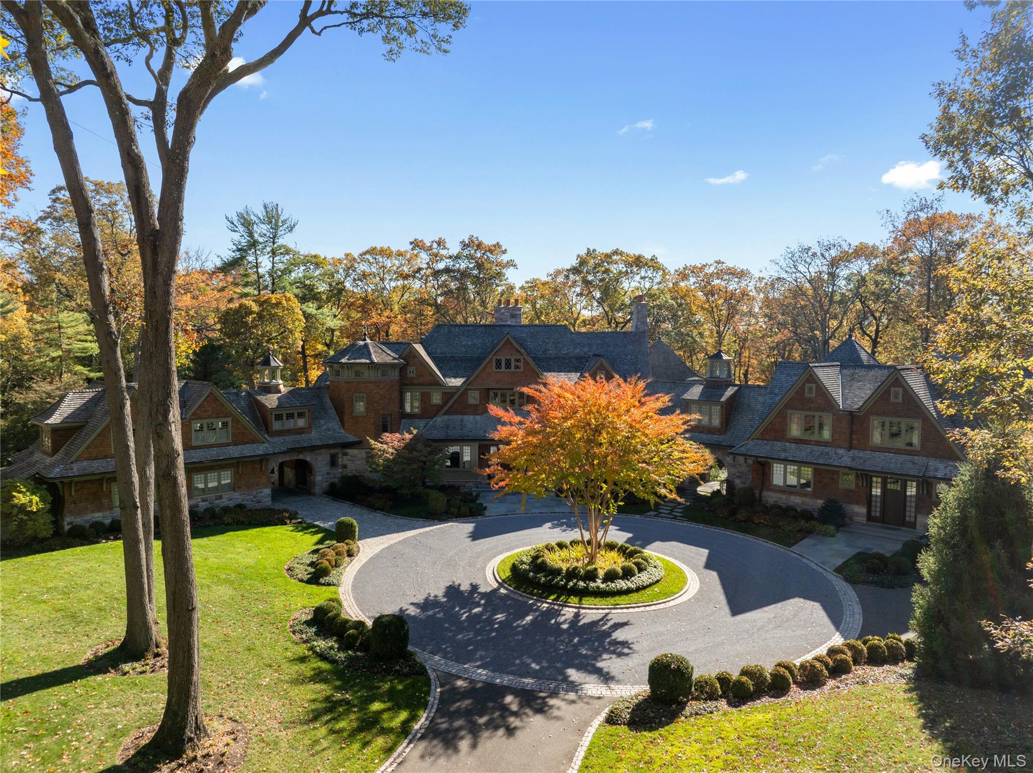 Tucked away in the prestigious Village of Mill Neck, this gated estate, built in 2012, is a true masterpiece of design and craftsmanship. A long, sweeping circular drive leads to the striking North Shore residence, whose timeless exterior blends hand-laid stone and copper gutters with classic shingle architecture. A semi-attached guest residence, connected by a covered breezeway, enhances the sense of privacy and versatility - creating a gracious compound that balances sophistication with relaxed luxury.

Every inch of the home reflects uncompromising quality and attention to detail. Loewen windows, Hunter Douglas shades, Venetian plaster walls, and intricate natural woodwork enrich each space. Soaring ceilings, curved doorways, custom millwork, and exposed wooden beams highlight the home’s architectural refinement. Modern comforts include integrated speakers, a geothermal HVAC system, radiant heating and a full-house generator, while seamless air grates, handcrafted cabinetry, wide plank white oak flooring, hidden pocket doors, and arched niches add warmth and character.

At the heart of the residence lies a magnificent kitchen inspired by Christopher Peacock design, elegantly appointed with jade-hued countertops and professional-grade appliances. A sunlit, circular breakfast room, framed by soaring ceilings and walls of windows, provides a serene setting for relaxed gatherings. The gracious main level also includes a formal dining room with custom display cabinetry, a sunken great room with a grand stone fireplace and bespoke wet bar, a richly paneled office, two elegant powder rooms, and an exceptional pantry with a secondary refrigerator, all conveniently located near the mudroom and attached garage.

The primary wing serves as a private sanctuary, complete with its own foyer, fireside lounge, spa-inspired marble bath, and a spectacular dressing room with a center island. Upstairs, four additional bedrooms each feature custom wardrobe installations and luxurious en-suite baths. The second floor also includes a spacious bonus room currently serving as a full-service gym, a built-in beverage station with refrigerator, a powder room, a homework or craft alcove and access to the large, finished walk-up attic. 

The lower level offers endless opportunities for recreation and functionality, featuring a golf simulator/media room, glass-enclosed temperature-controlled wine cellar, game room, generous storage areas, utility rooms, and a commercial-scale laundry suite. A guest bedroom with an attached full bath completes this level.

Accessed via a covered slate walkway, the guest residence mirrors the same elegance on a more intimate scale. It includes a custom eat-in kitchen, spacious living room, welcoming foyer with powder room, and its own garage. The primary suite features a walk-in closet and private bath, complemented by two additional bedrooms, two full baths, a sitting room, and a finished lower level with laundry and flexible recreational space.

Outdoor living is equally exceptional, offering multiple stone terraces - including a fully covered entertaining area with fireplace - a porte-cochere, and an outdoor kitchen with its own, secluded privet trimmed patio. The rolling, picturesque lawns are beautifully landscaped with specimen trees, professional lighting, an enclosed vegetable garden, and a private putting green with a 85-yard practice range.