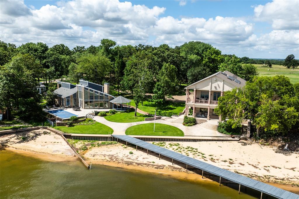 Nestled on a protected water cove and iconic spot in prestigious gated Beachwood Estates, this exceptional 3.746-acre waterfront retreat at Cedar Creek Lake offers the perfect combination of privacy, space and unforgettable lakefront living. Lovingly enjoyed by the same family for over 20 years, the property is designed for gathering, relaxing and creating lasting memories. The estate comfortably sleeps over 20+ guests across three separate residences, making it ideal for extended family, corporate retreats or large group getaways. The impressive main residence encompasses 4,762 square feet and features four bedrooms - each with its own private bathroom, two full kitchens, a four-car garage and two inviting living areas with fireplaces. A large game room equipped with a full bar, shuffleboard, table tennis and pool table provides the perfect space for entertaining and unwinding after a day on the water. The charming A-Frame house offers 2,389 square feet of living space with three bedrooms and two bathrooms. The living room features a dramatic wall of windows showcasing breathtaking views of the lake and sparkling pool. An attached deck and lakeside gazebo create the perfect setting for morning coffee or evening sunsets. The small guest house adds additional flexibility with approximately 400 square feet, a large bunk room, full bathroom attached deck and an attached two-car garage. Outdoors, the property transforms into a true lakeside resort. With over 100 feet of shoreline, the property also features a private dock and boat house with lift, offering easy access to boating, fishing and all that Cedar Creek Lake has to offer. Located just an hour drive from Dallas, this rare property also allows short-term rentals, creating an incredible opportunity for those looking for a vacation retreat or income-producing lake front property. Best of all, the property comes completely furnished.