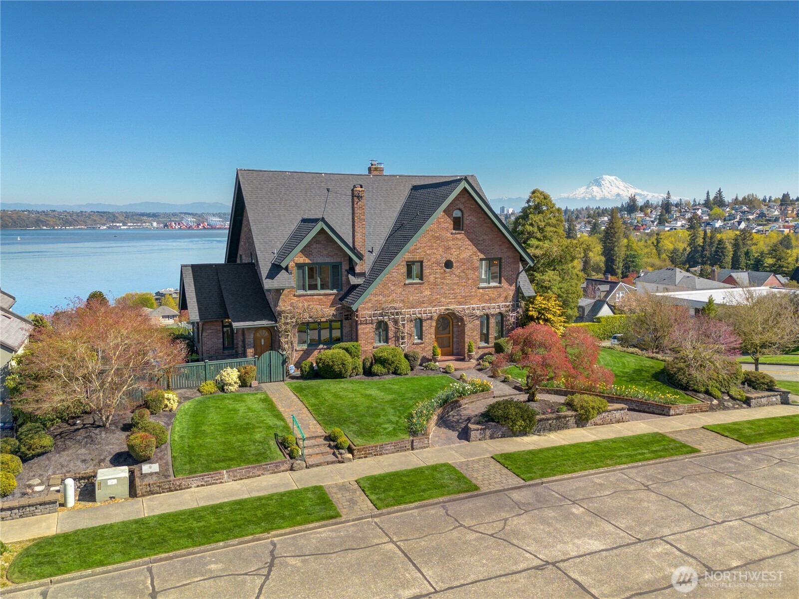 Some homes are built to endure. Perched on one of North Tacoma's most coveted streets, this landmark 1925 all-brick estate commands arguably the finest panoramic view in Tacoma — Commencement Bay, Mt. Rainier, and the Cascade Mountain Range, framed from your living room, dining room, and private upper terrace. Grand arched windows flood the interior with light and water views at every turn. Hardwood floors, original millwork, soaring ceilings, and two gas fireplaces speak to craftsmanship that simply cannot be replicated. Five bedrooms, 3.5 baths, and 5,723 square feet of grand entertaining spaces flow seamlessly to stone terraces, exceptional gardens, and a private sport court below. From the first light rising over the Cascades to the last glow fading over Commencement Bay — every moment at this address is defined by the view. A new roof, completed pre-inspection repairs, and decades of meticulous maintenance mean nothing left to discover — only the opportunity to put your own signature on a home built to last another hundred years. Minutes to Proctor District, Annie Wright Schools — ranked #1 private K–12 in Washington State — and the historic Tacoma Lawn Tennis Club. For the family planting roots, the executive seeking a statement address, or the legacy buyer who understands that views, brick, and character like this come to market perhaps once in a decade — this is that home.