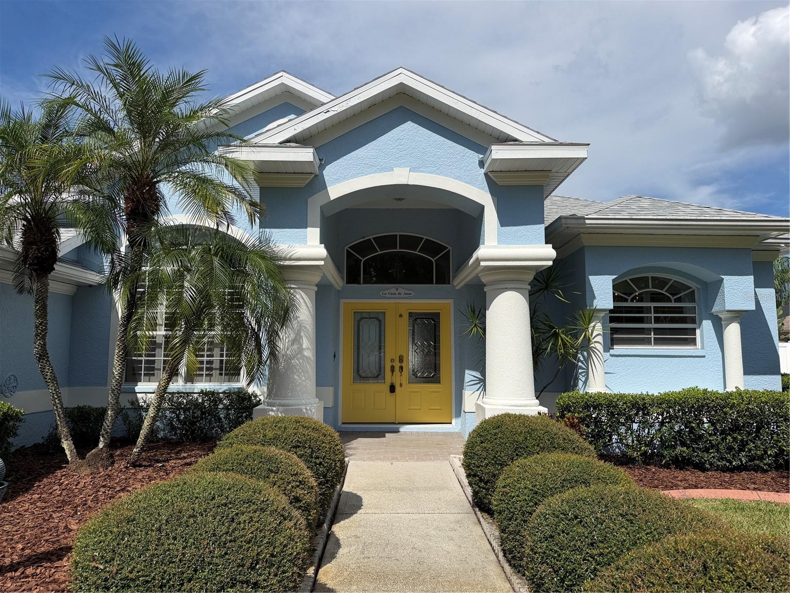 Welcome to La Casa De Amor, a house you’ll love. This Popular floor plan brilliantly brings natural sunlight into the home. Stained glass doors at the front entry and a large overhead transom window combined with the 3 pane sliding glass doors contribute to the happy character of this home. Stepping into the grand entrance you will appreciate the size of the living room measuring 17ft by 22 ft. The great room keeps you connected with friends and loved ones. Off to the left is the formal dining area with a considerable window and plantation shutters that face South. The living room has a dividing wall near the kitchen that tucks away part of the kitchen from view, however the rest of the kitchen which includes a breakfast bar is in full view of the living room. This functional split floor plan has 2 bedrooms and a bonus room, indoor laundry, guest bathroom and garage on the West side of the home. The primary bedroom & ensuite span the East side of the home. High ceilings with crown molding, three extravagant windows with drapes & sheers are features of this spacious 13.5 x 15ft bedroom. There is plenty of closet space with a super-sized walk-in closet, ample shelving and direct access to the attic; plus, a 2nd closet in the primary bedroom, and then a linen closet in the bathroom. Expansive luxury bathroom is equipped with a double vanity & make-up station, jet tub with an overhang chandelier, separate shower with built in seat, 2 shower heads and 3 jets, and a private water closet with a window facing East. Both the 1st and 2nd bedrooms have window seats, ceiling fans with light kits, built in closets with above-mentioned alcoves for showcasing collectables. Laundry room has a sink, a rod for hanging clothes, cabinets & washer/dryer. Bonus room is a designed space ideal for a home office at 16 ft wide by 7.6 ft in length. 2 car garage houses water softener, irrigation system, breaker panel and access space to attic. Guest bathroom has a toweled shower with tub, quality glass sliding doors, a pedestal sink and a door that exits to the lanai. There are two outdoor showers one at the West side of the home near the office and one under cover at the lanai. The extra-large lanai has two ceiling fans with lights, a flat screen TV under roof, lots of pavers, and two exits to the backyard. The backyard has vinyl fencing for complete privacy.  On the East side of the property there is a putt putt golf area with fake turf that could use some TLC. The HOA takes care of the mowing and edging of the front and back lawn giving you more time to spend at the pool and perhaps playing water volleyball with the residences on the weekends. If your concerned about the electric bill don’t be; The home has solar panels installed on the West end of the home and in 2024 a 3.5-ton 15 Seer HVAC system was installed that has a warranty for 12 years for parts, and unit replacement of the compressor for first 6 years. This home is situated at a prime location within the community. There is a gate in the backyard that leads directly to the club house, pool, hot tub, tennis and pickleball courts. This private boutique community allows residents to enjoy social nudism at the pool, hot tub, pickleball courts and clubhouse. In the surrounding area there are two public golf courses, local restaurants, doctors’ offices and shopping malls. Multiple nudist resorts are within 1 ½ miles to 6 miles from the community and Tampa International Airport is about a 25 minute drive.