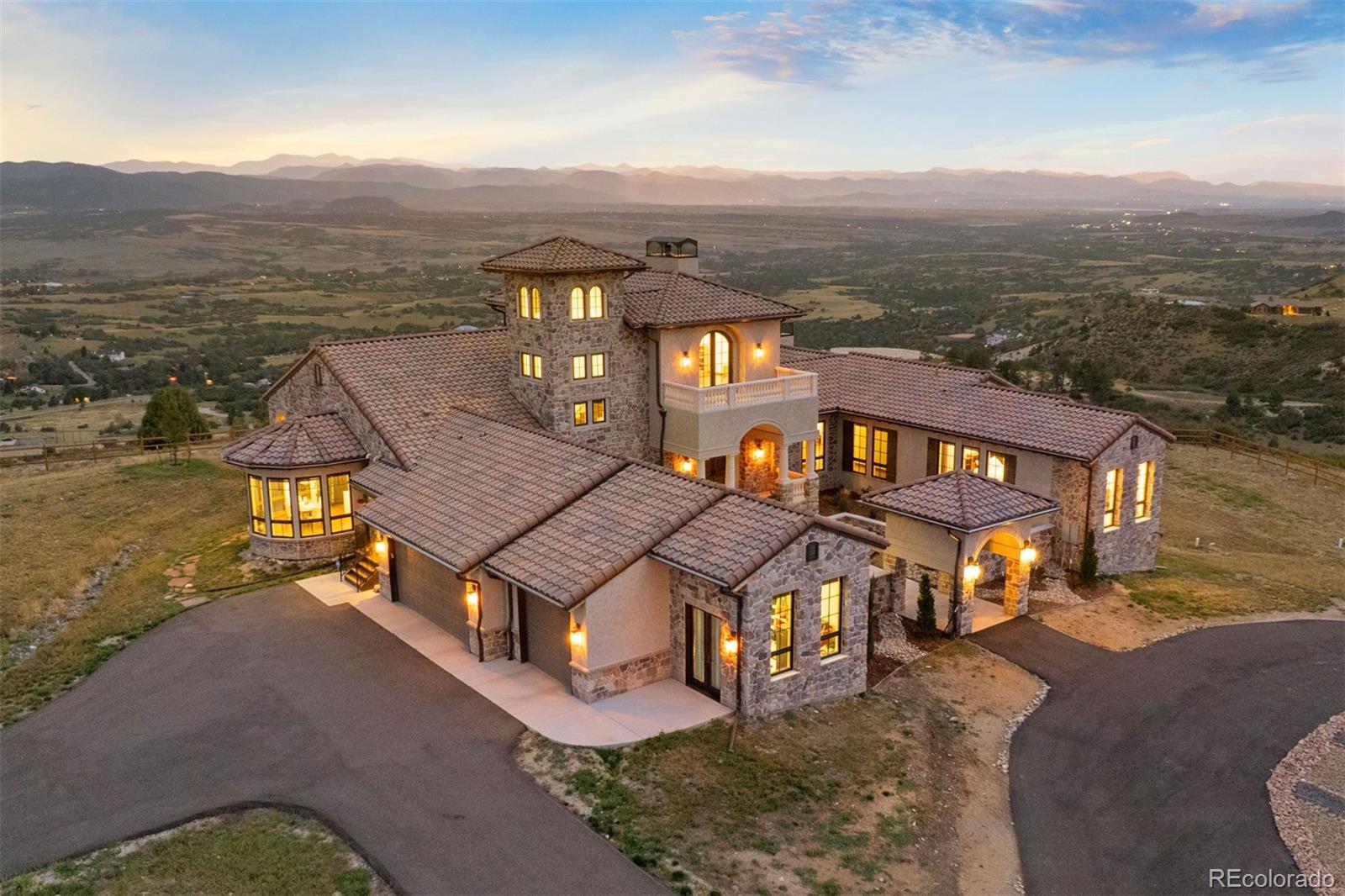 Some homes feel like a destination—this one feels like a calling. A place that pulls you in with its stillness, holds you with its design, and feels both transported and deeply rooted in its setting. Set atop a secluded mesa with dynamic topography and a private pond, this newly built Mediterranean-inspired estate offers an extraordinary vantage point, with the entire Front Range, Pikes Peak to Longs Peak, visible from every window. On over 35 acres in one of Castle Rock’s most exclusive gated communities, the home draws from authentic Italian architecture: stone arches, a courtyard, and stately columns that define its expansive outdoor living spaces. Feels like Italy. Looks like Colorado. Lives like nowhere else.Symmetry is a hallmark of the design, creating balance and rhythm, and it all converges in the great room. Vaulted ceilings with beams, towering arched doors, and a cast concrete fireplace bring proportion and warmth, while expansive windows frame the ever-present mountain backdrop. The kitchen is anchored by two oversized waterfall islands and surrounded by floor-to-ceiling cabinetry, JennAir appliances, and thoughtful touches like a built-in Miele coffee maker and Italian wine window. Outdoor spaces are designed for year-round use, with arched stone columns, a curved viewing balcony, tongue-and-groove ceilings, and a lower patio wired for a hot tub.Main-floor living includes a mountain-view primary suite with private balcony, a two-sided fireplace, spa-worthy bath, and expansive walk-in closet. A guest suite, office, and mudroom with pet wash add everyday ease. Above, the crow’s nest offers a flex space with twin balconies—ideal for work, creativity, or quiet retreat. The walkout lower level features a recreation room with fireplace, wet bar, gym, and 2 bedrooms. And through it all, with the kind of quiet that only comes from open land and long views, it lives like the Italian countryside—but looks out over Colorado’s most iconic skyline.