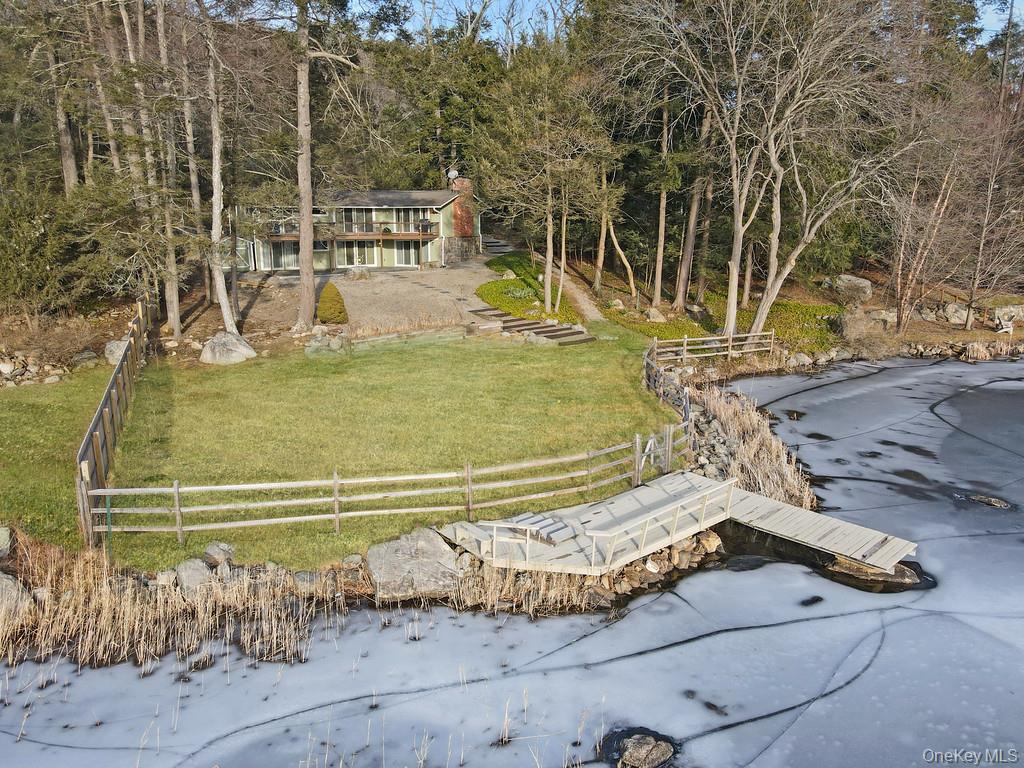 Set along the shoreline of Lake Oscaleta, this direct waterfront home offers a rare combination of privacy, natural beauty, and truly usable lakefront property in the heart of South Salem. Occupying .564 acres with sweeping frontage on one of the area’s most peaceful glacial lakes, the setting is defined by something increasingly hard to find - an expansive, level lawn that extends all the way to the water. Unlike many lakefront properties where steep slopes limit access and usability, this property offers a broad, open yard ideal for entertaining, recreation, or simply enjoying the outdoors. The gentle approach to the lake creates an effortless connection between the home and the water, making everyday use as practical as it is beautiful. At the shoreline, a substantial private dock and swim platform provide immediate access to the lake, whether for launching kayaks and paddleboards or spending long summer days in and around the water. Lake Oscaleta is known for its depth and quiet character, with limited motorized use that preserves its calm, reflective setting. The home itself has been thoughtfully updated and is designed to maximize its connection to the lake. The main level, offering approximately 1,578 square feet, is centered around an open living and dining space with vaulted, wood-beamed ceilings and a striking brick fireplace that anchors the room. Walls of glass and sliding doors frame the water from nearly every angle, filling the home with natural light and providing seamless access to the expansive deck - perfect for dining, entertaining, or simply taking in the view. The kitchen integrates comfortably into the living space, creating an easy flow for both everyday living and gatherings. The primary bedroom enjoys direct access to the deck and lake views, while two additional bedrooms and well-appointed baths complete the main level. The home is also equipped with an automatic whole-house generator, providing peace of mind and uninterrupted comfort year-round. The full walkout lower level adds approximately 1,200 square feet of flexible living space, ideal for guests, recreation, or extended stays. With its own fireplace, multiple seating areas, and direct access to the stone patio and backyard, it functions as a true extension of the home, offering both comfort and versatility. Outside, the landscape has been designed to complement the natural setting, with a combination of lawn, stonework, and mature trees creating multiple outdoor living areas without sacrificing the openness of the yard. From the elevated deck to the covered patio below, every space is positioned to take advantage of the lake. Just minutes from the hamlets of South Salem and Ridgefield, and within easy reach of Metro North and major highways, this is a property that offers both escape and accessibility. A rare opportunity to own a level, highly usable waterfront property with a substantial dock on one of Northern Westchester’s most serene lakes.