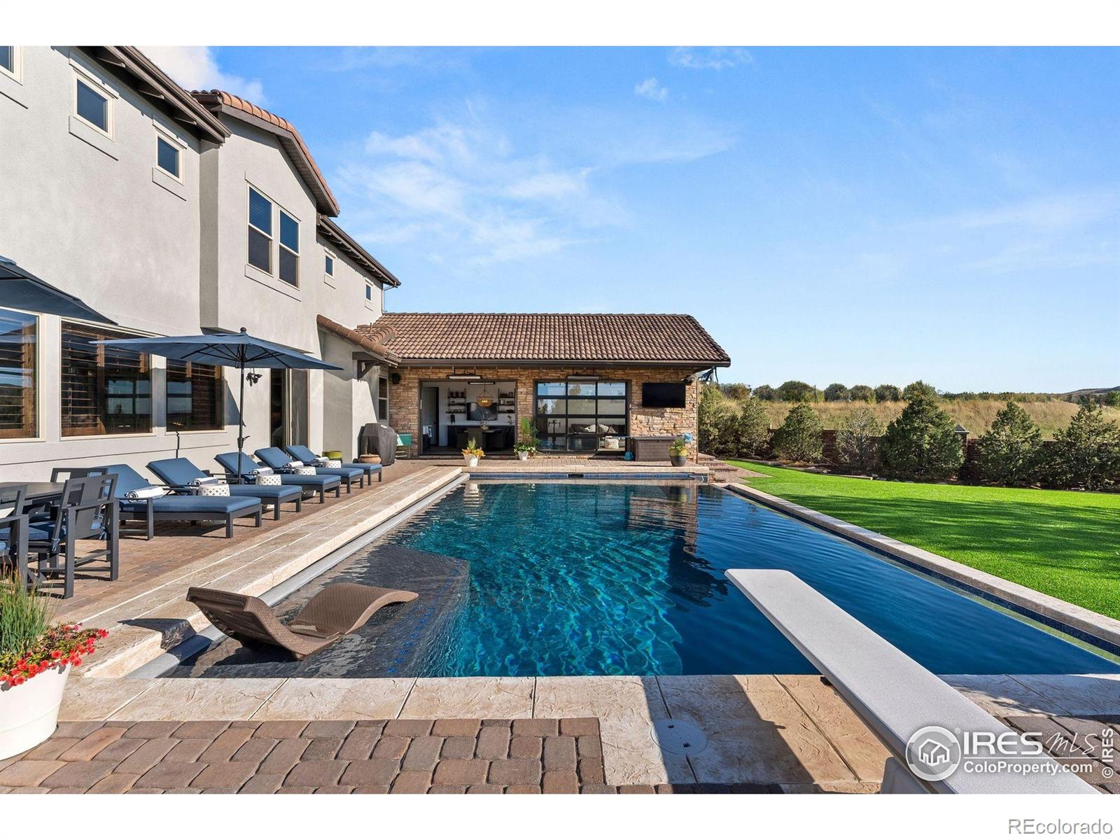 Sited on one of the premier lots in all of Heritage Hills, this fully loaded residence redefines luxury living with over $1 million in bespoke upgrades and a jaw-dropping pool house addition completed in 2022. Perfectly positioned on an oversized, west-facing cul-de-sac lot (originally the highest lot premium in Overlook), the home captures unforgettable mountain views and sunsets. Anchored by a resort-style infinity-edge pool and hot tub, the pool house includes an incredible spa-like shower bath, wet bar and private laundry creating an entertaining space that's as functional as it is stunning. The thoughtfully designed outdoor setting also features low maintenance turf, a built-in firepit, and expansive patios designed to take full advantage of the incredible view. At the heart of the home is a dramatic central courtyard that connects seamlessly to the interior and offers year-round enjoyment with its built-in grill and custom stone fireplace. Inside, every surface was thoughtfully selected-high-end reclaimed oak floors, knotty alder doors and shutters and extensive custom cabinetry. The central kitchen is beautifully appointed with professional-grade KitchenAid appliances, highly upgraded granite countertops and a custom walk-in pantry The main level also includes a custom office, a 2nd office or "project room" with abundant cabinetry, and a front entry expansion that allows interior access to both garages-each finished with epoxy floors and custom cabinetry. Upstairs, the luxurious primary suite offers breathtaking mountain views, a spa-caliber primary bath, and a walk-in closet that connects directly to the upstairs laundry. Three additional ensuite bedrooms and a spacious loft with custom built-in desks complete the upper level. The finished basement impresses with a 120" theater, a decked-out bar, a private 5th bedroom, a gorgeous shower bath, and a 275-square-foot fitness space. This one-of-a-kind Heritage Hills estate delivers an elevated Colorado lifestyle