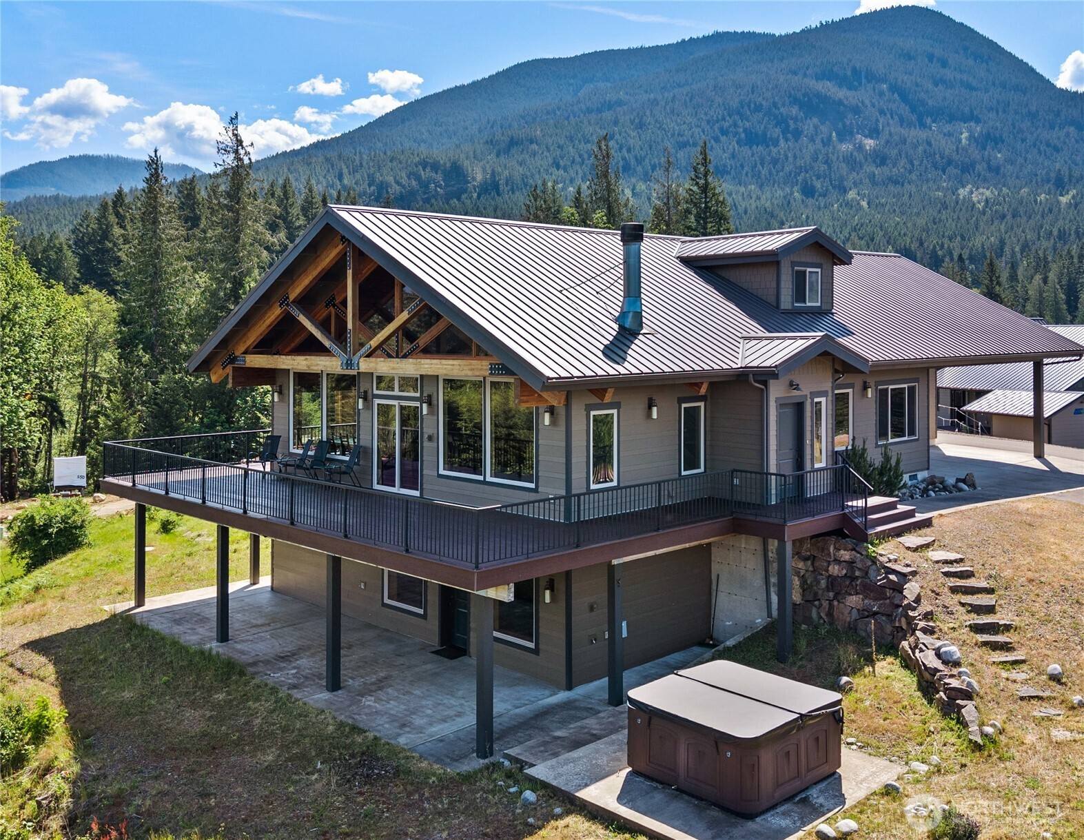 Perched atop the hill in Packwood’s arguably most coveted gated community, Hideaway Estates offers the kind of sweeping 360° mountain and valley views that stop you in your tracks. This custom-built retreat was designed to bring the beauty of the Northwest indoors, with soaring open beams, warm bamboo floors, and expansive windows framing the ever-changing landscape.   The inviting great room flows into a luxury kitchen featuring rich alder cabinetry, matte granite slab countertops, and generous gathering space for entertaining after days spent exploring nearby mountains, rivers, forests, and ski slopes.   Step outside to the view deck for seamless indoor-outdoor living surrounded by clean mountain air, abundant wildlife, and peaceful natural beauty. With two spacious primary suites plus two bunk rooms, each with its own ¾ en-suite bath, there is room for everyone to relax in comfort.   A second living room on the lower level also captures stunning mountain views and opens to a patio with hot tub—perfect for unwinding beneath the stars. Built-in Desco sound system, two 50-gal water heaters, attached garage and carport, oversized custom laundry room, and natural low-maintenance landscaping complete this exceptional mountain home. Just a short drive from Mount Rainier National Park and White Pass Ski Area, this is Northwest mountain living at its finest.