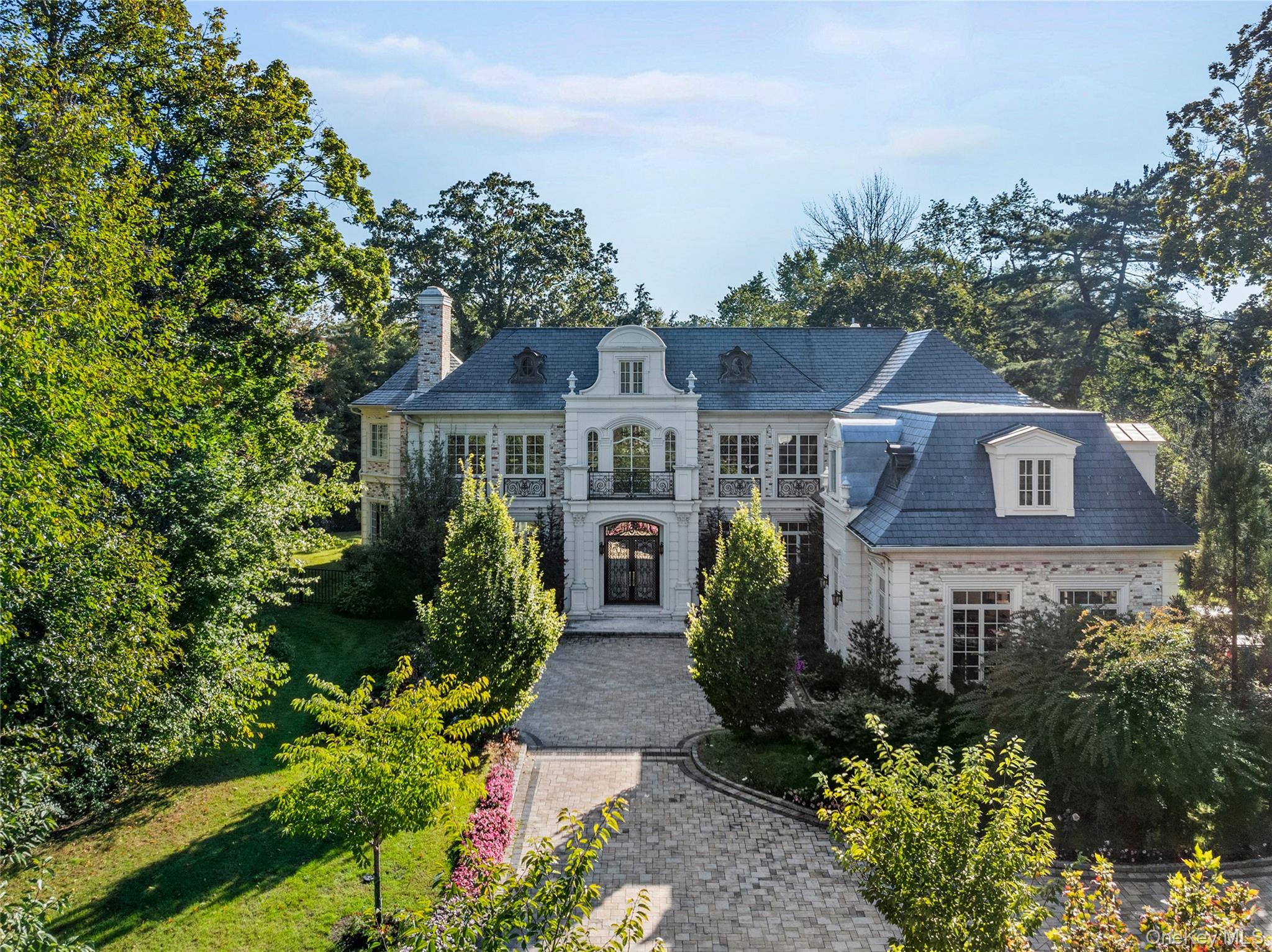 Welcome to 6 Foxwood Road, an extraordinary Colonial estate nestled in the heart of Kings Point, NY. Constructed in 2021, this all-brick and solid stone masterpiece is situated on over one acre of impeccably landscaped grounds, featuring an expansive stone patio, a luxurious in-ground gunite pool, hot tub, and a fully equipped outdoor kitchen - ideal for elegant alfresco dining and effortless entertaining.

Showcasing approximately 8,000 Sq.Ft. of meticulously designed living space, the home offers a dramatic formal layout adorned with soaring ceilings, rich hardwood floors, and impeccable custom finishes throughout. A grand marble foyer with a sweeping bridal staircase sets the tone for refined living, while the formal dining room, complete with a bespoke built-in display case, adds a touch of timeless sophistication.

The striking blue high-gloss kitchen is a chef’s dream, equipped with a full suite of top-of-the-line, professional-grade appliances and a polished, mirrored Butler’s Pantry. A beautifully curved, designated office space offers a stylish and functional workspace, while the oversized family room, featuring chevron-patterned hardwood floors, opens through French doors to the expansive rear patio, which spans the entire length of the home. This seamless indoor-outdoor flow creates a spectacular setting for grand-scale entertaining or tranquil relaxation. Multiple oversized gas fireplaces infuse warmth and character into the living spaces, while Venetian plaster ceilings and thick-cut millwork elevate the home’s refined aesthetic.

The lavish primary wing serves as a private sanctuary, complete with a dedicated vanity area, multiple outfitted walk-in closets, and a spa-inspired en-suite bathroom. A stunning circular glass-enclosed shower serves as the centerpiece, beautifully complemented by a freestanding soaking tub and exquisite marble finishes.

This designer residence features 6 spacious bedrooms, 5.5 luxuriously appointed bathrooms, radiant heated floors, a full-house generator, a finished attic space, and a large unfinished basement with tall ceilings, offering endless customization potential. An attached three-car garage completes this exceptional offering - a true statement of luxury living on a waterfront street within the sought-after Great Neck Union Free School District, zoned for North schools.