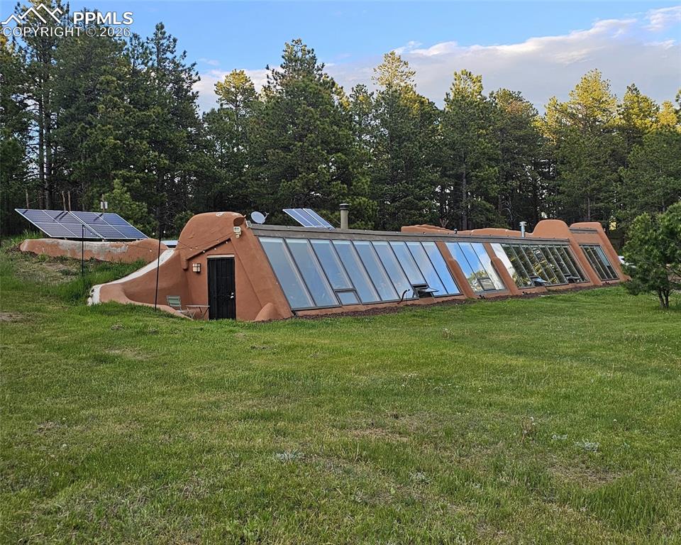 An exceptional, rare Earthship retreat awaits in the heart of Black Forest. Nestled among trees this off-grid, solar-passive home on 5 private, peaceful acres offers a self-sustaining lifestyle without sacrificing comfort or modern convenience. With over 2,900 sq ft on a single level, the home is thoughtfully designed to maintain a comfortable climate year around while being completely independent from public utilities. A dramatic 100-foot wall of windows anchors the front of the home, flooding the expansive interior with natural light. An indoor pond and wall of built-in planters complete with drip irrigation bring nature seamlessly indoors. The spacious kitchen is a standout, featuring abundant cabinetry, a generous walk-in pantry, slate backsplash, extensive counter space, brand new propane powered refrigerator and large dining space. Energy efficient with fully owned new solar system, an automatic propane generator, on-demand tankless water heater, and 2 heating options; cozy gas-burning stove and a brand new pellet stove. Utility costs remain impressively low. High-speed fiber optic internet, offering lightning-fast connectivity even in this serene, rural setting. The bathroom is both functional and artistic; large windows, a deep tub, double vanity, a stained-glass door, and a wall of embedded glass bottles that cast beautiful, colorful light in the space. The great room invites relaxation with large seating area, abundant sunlight, and sweeping views of the property. The primary suite is a retreat with walk-out access to the side patio, planters, a comfortable sitting area, and a walk-in closet. A flexible guest room offers a cozy recessed bed and a built-in planter wall that provides privacy and character. Additional highlights include an attached 2-car garage, a domestic well with a 500-gallon storage cistern and dedicated solar panels, an outbuilding, and land suitable for horses, animals, or RVs. With no HOA, the property offers freedom and versatility.
